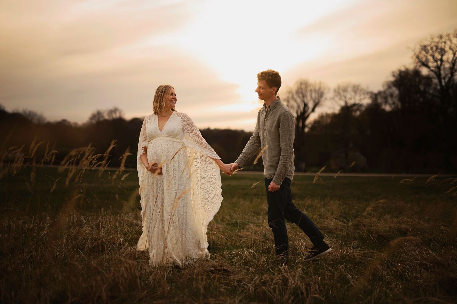A couple walks hand in hand through a field at golden hour with bride wearing flowing white dress.