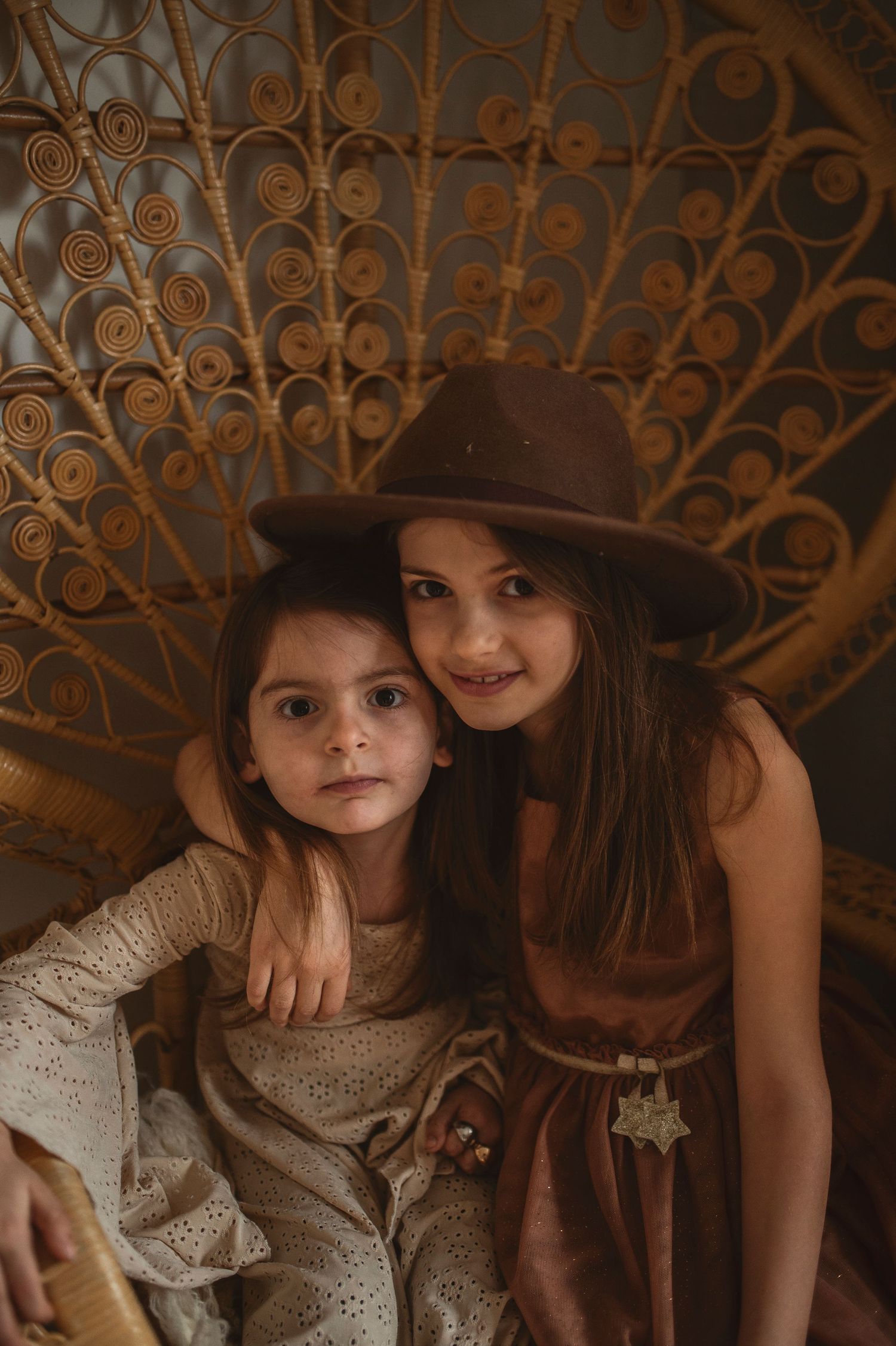 Two figures in vintage-inspired dresses pose together against an ornate woven backdrop.