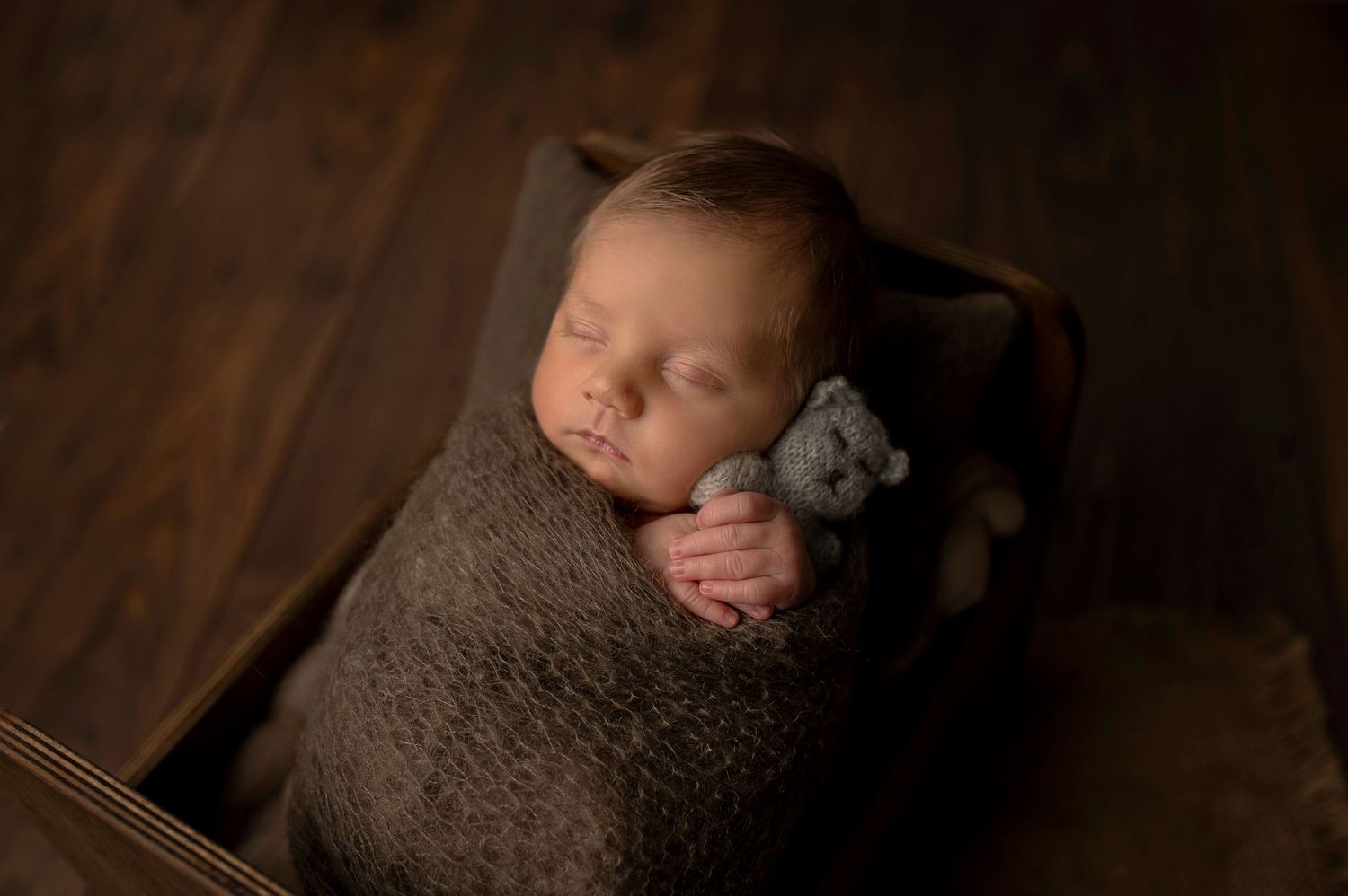 Nyföddfotografering i Hässleholm med en sovande bebis i brun filt och nalle i korg.