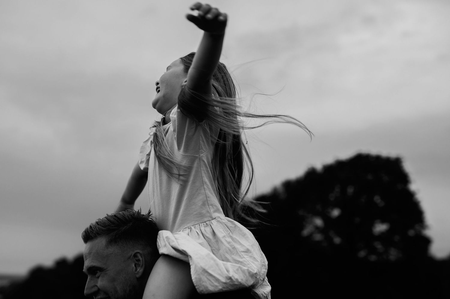 Familjefotografering i Skåne med barn som sitter på axlar i lekfullt svartvitt porträtt i naturen.