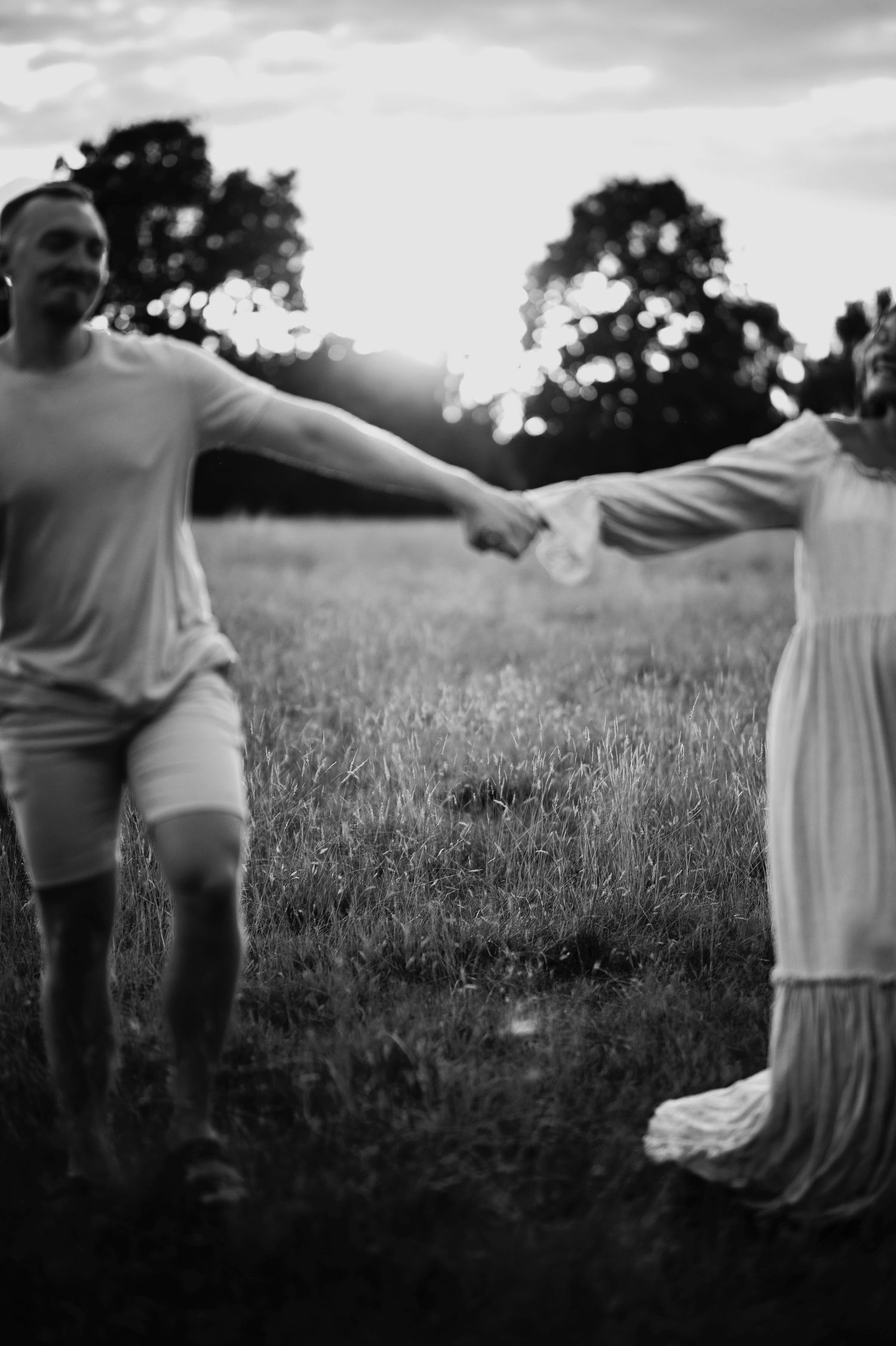 A black and white photo of a couple playfully holding hands in a field.