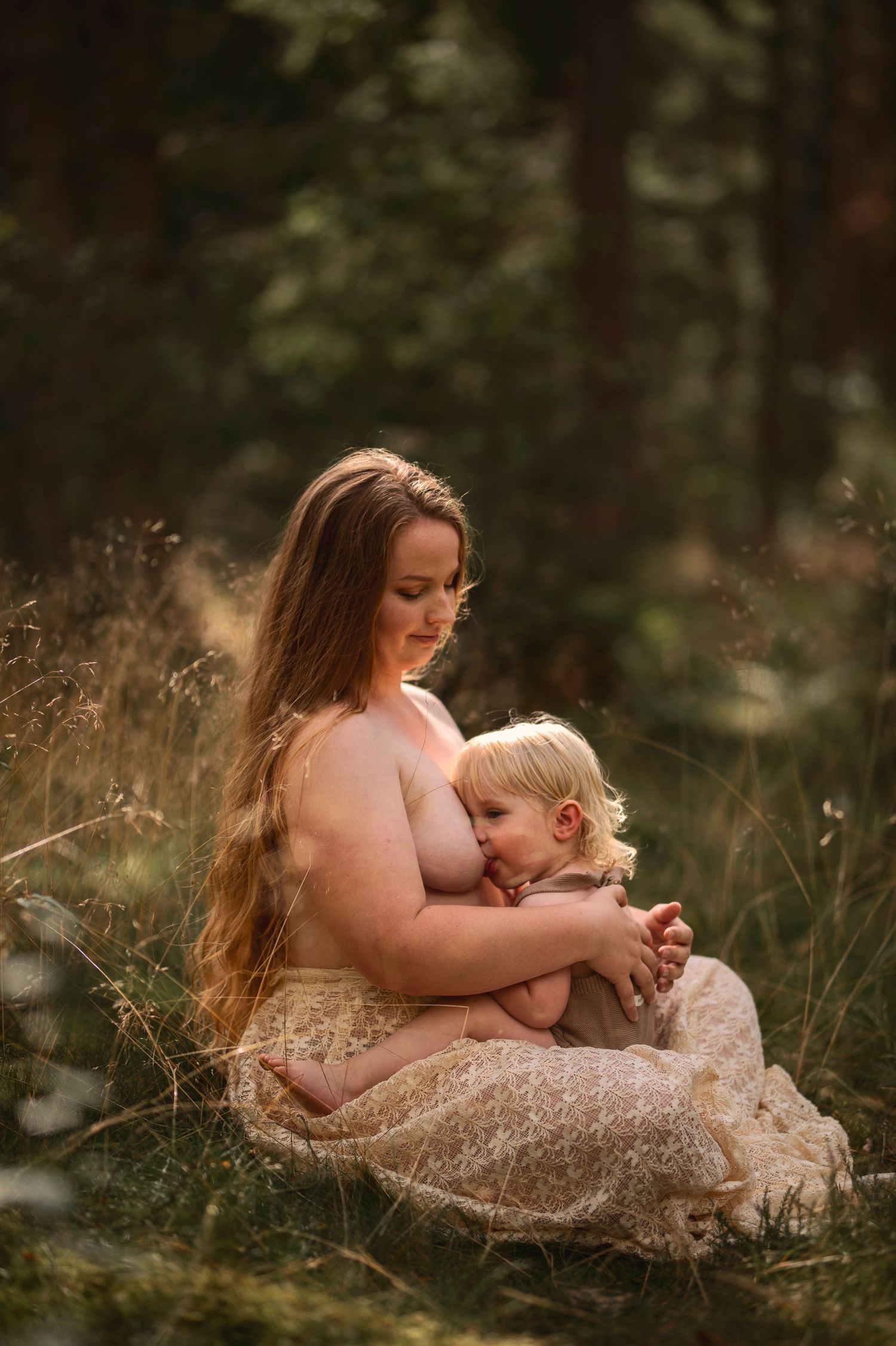 Moderskapsfotografering i Skåne med förälder som håller ett litet barn i spetsklänning i drömlik skogsmiljö.
