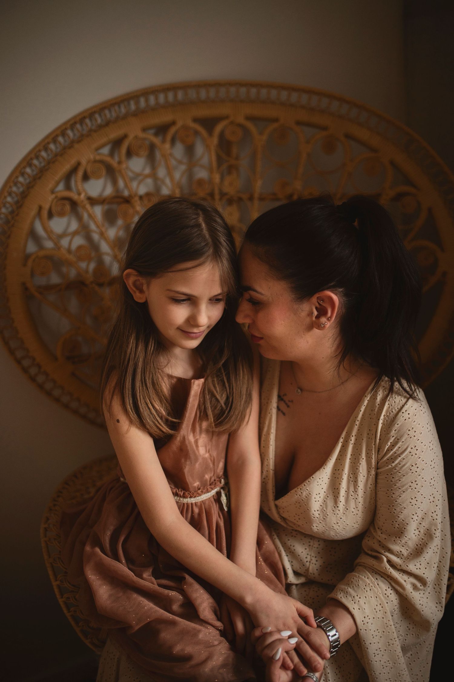 Tender moment captured in warm tones against ornate woven chair backdrop.