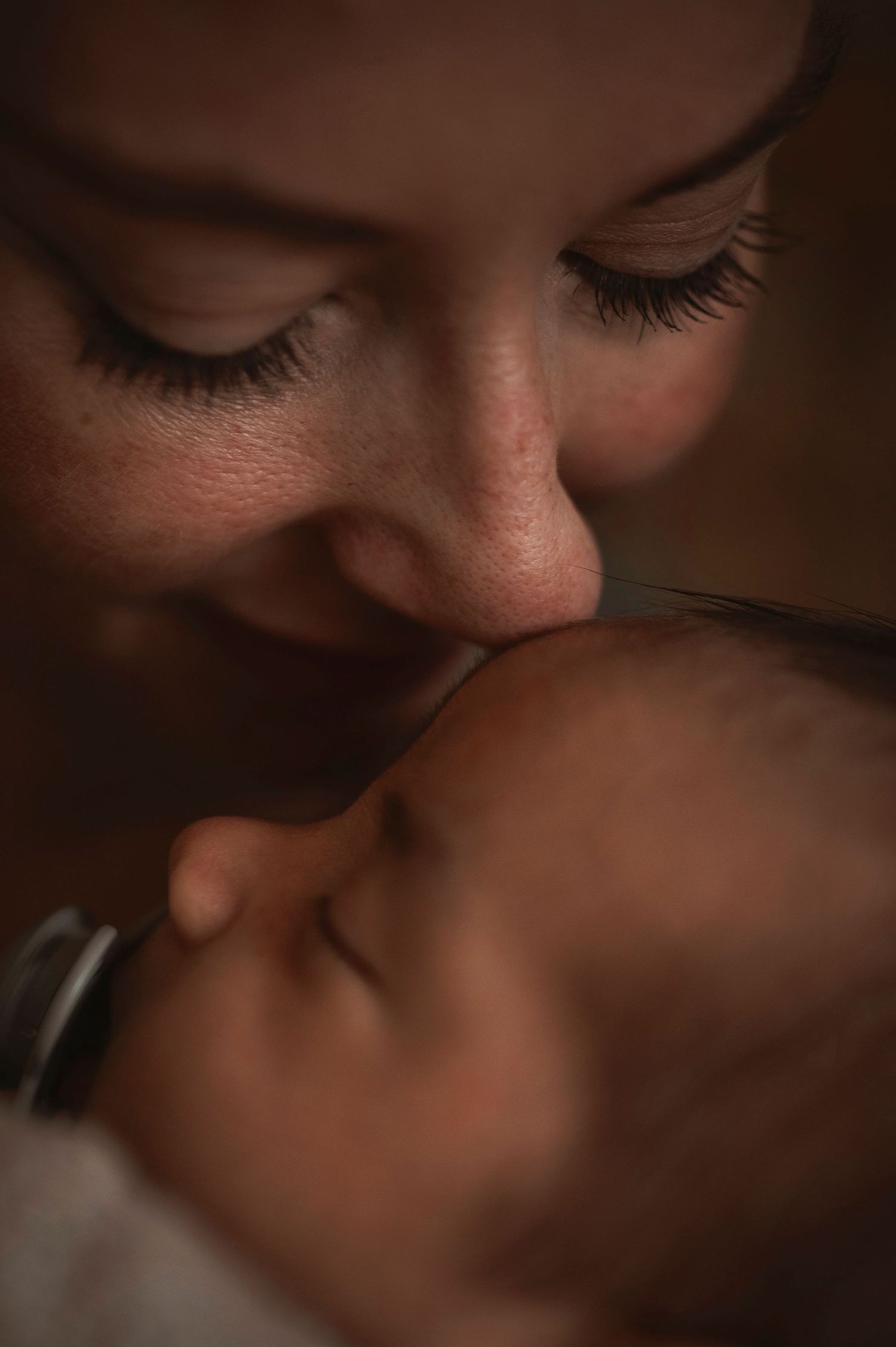Close-up intimate portrait showing gentle nurturing moment between parent and infant in warm lighting.