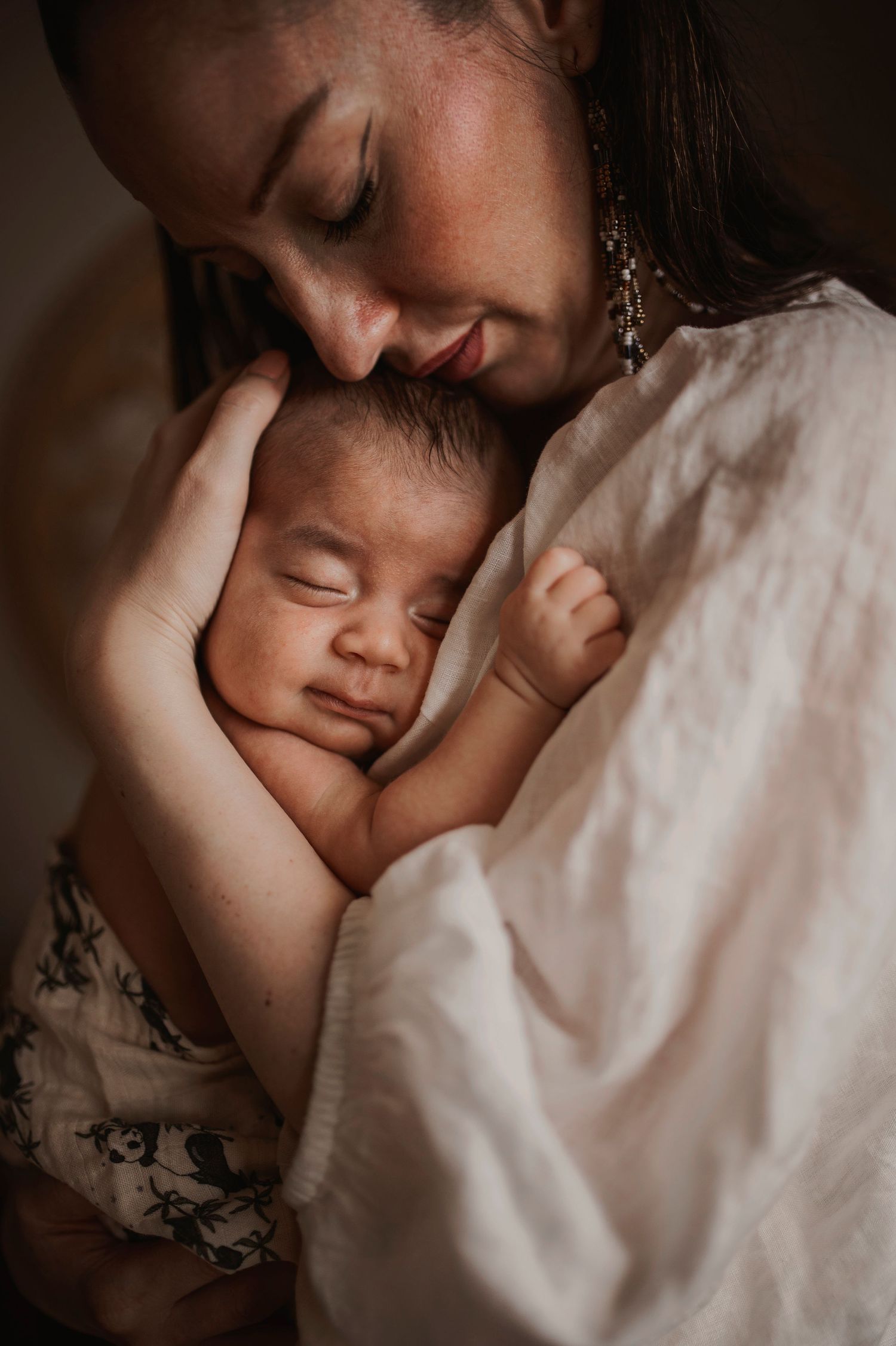 A tender moment captured between parent and sleeping baby in warm intimate lighting.