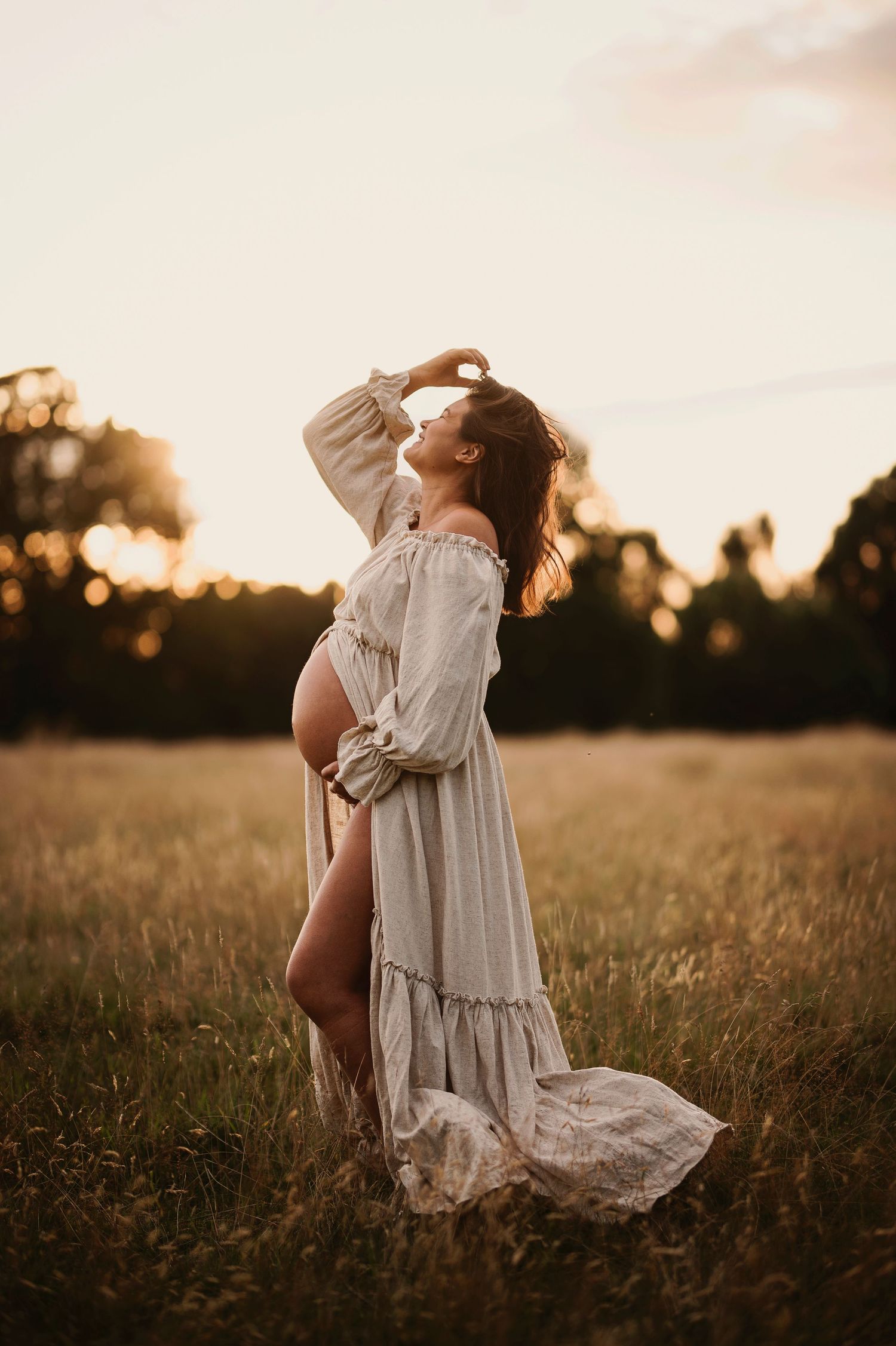 A dreamy maternity photo with a long white dress in a sun-drenched field.