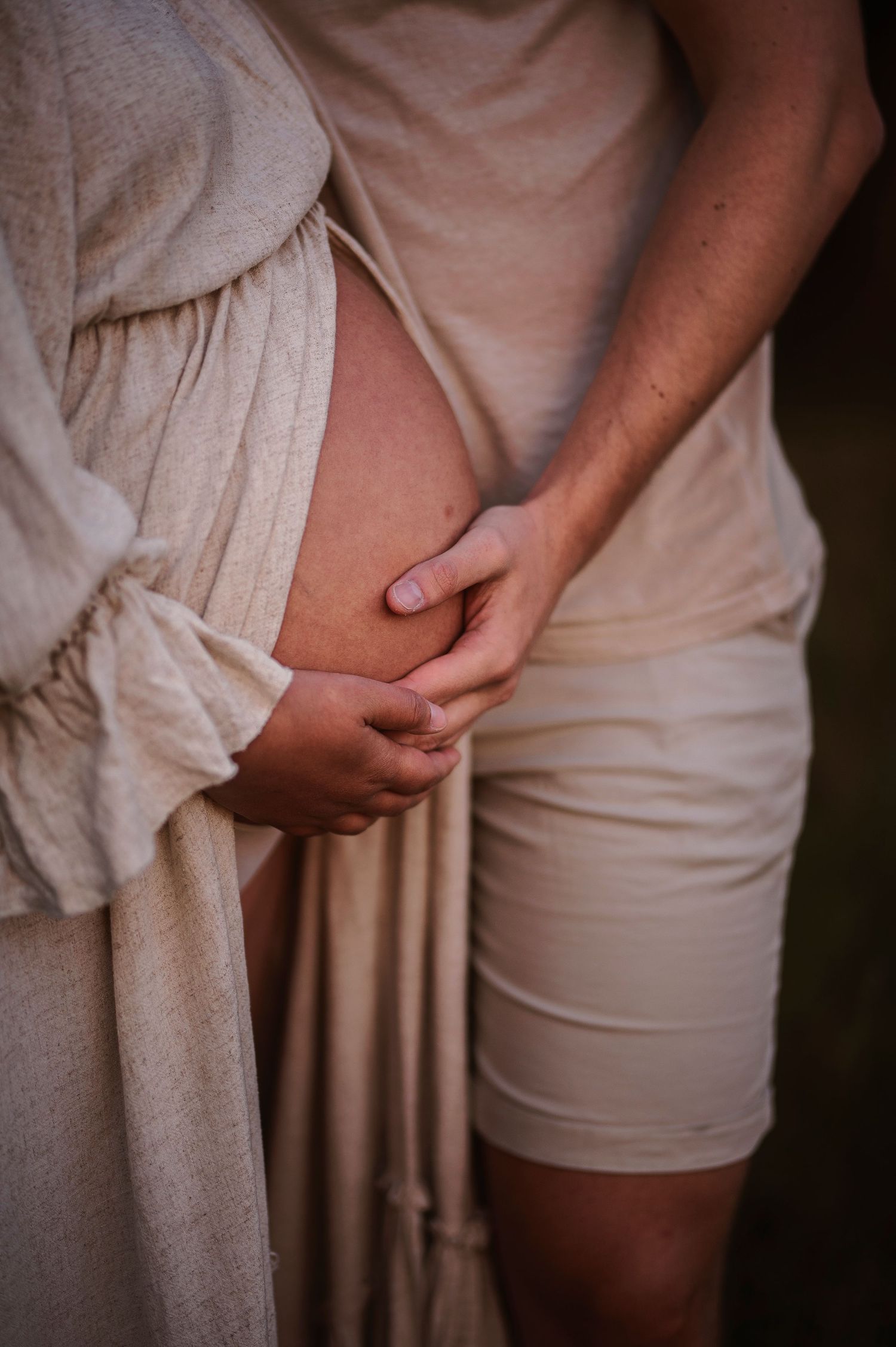 Close-up of hands gently cradling a pregnant belly in soft lighting.