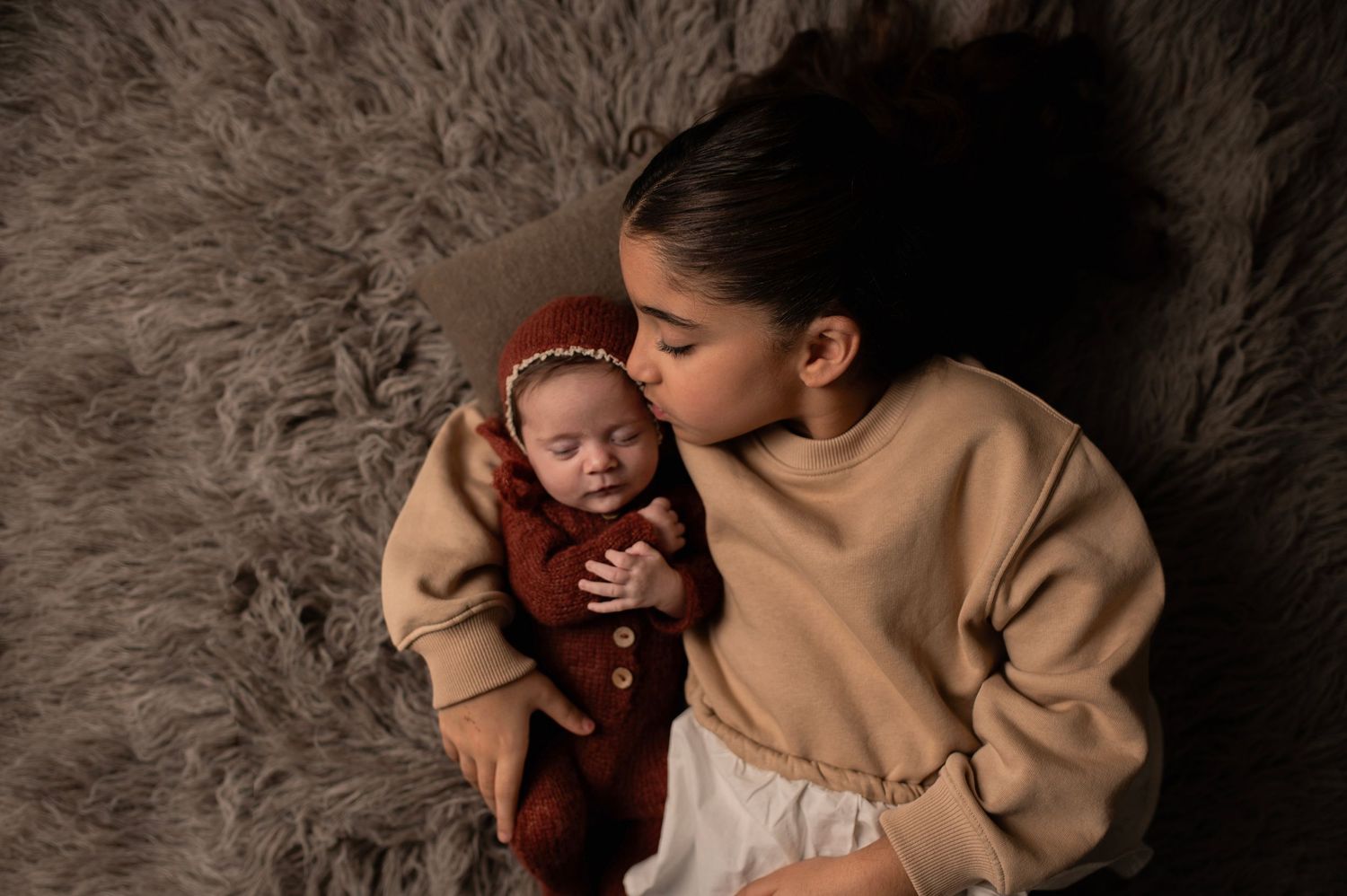 Parent and baby in matching tan sweaters laying on plush grey carpet.