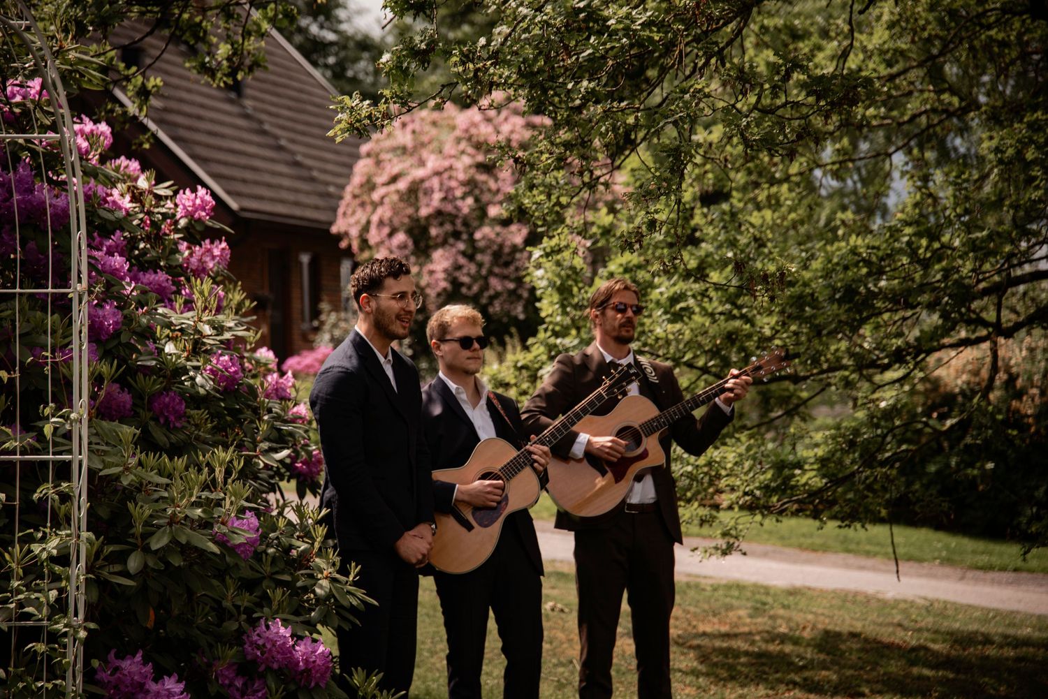 Eventfotografering i Skåne med tre musiker som spelar gitarr utomhus i blommande miljö.