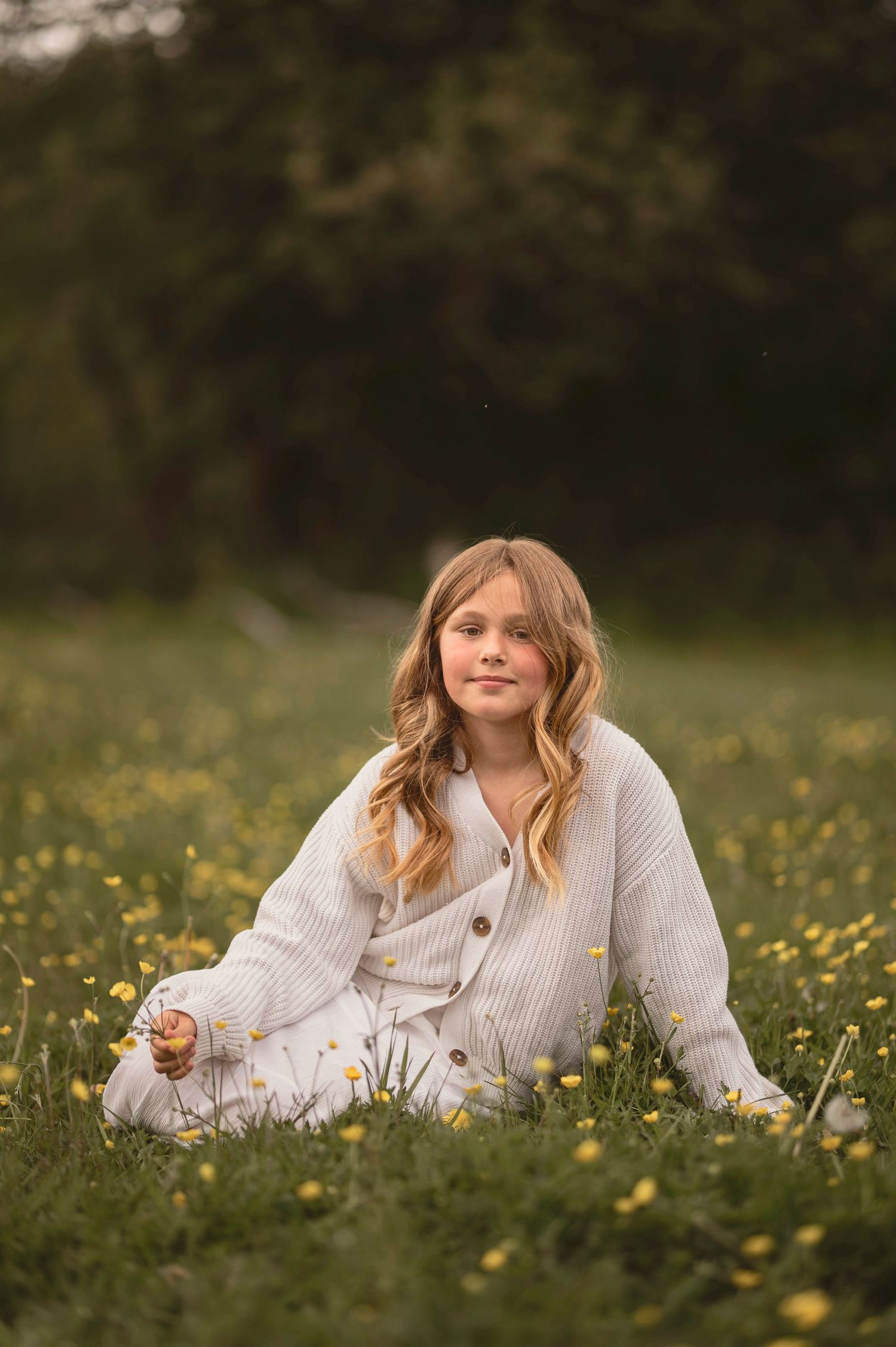 Barnfotografering i Skåne med flicka i vit kofta i gul blomsteräng i gyllene kvällsljus.