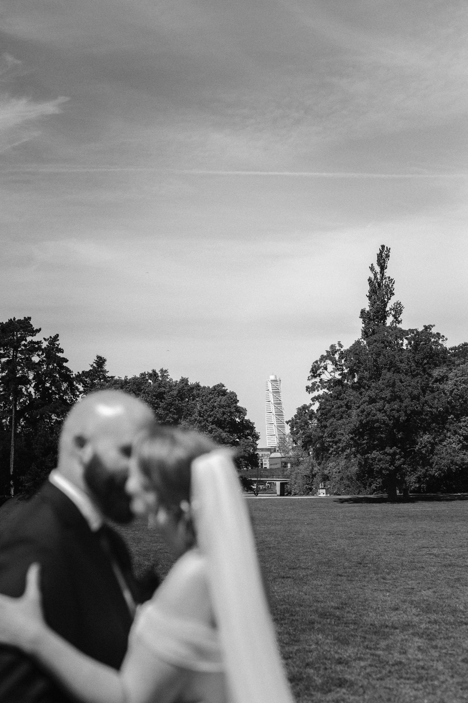 Bröllopsfotografering i Malmö med brudpar som kysser varandra i park med Turning Torso i bakgrunden i svartvitt.