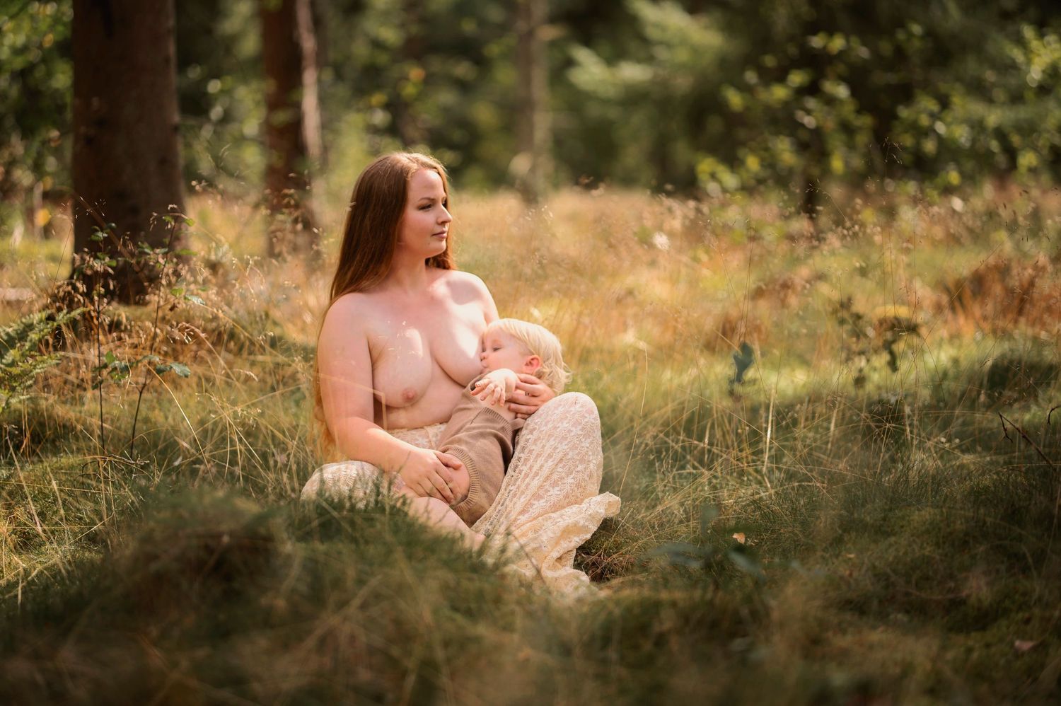 Moderskapsfotografering i Skåne med förälder som håller ett litet barn i spetsklänning i drömlik skogsmiljö.