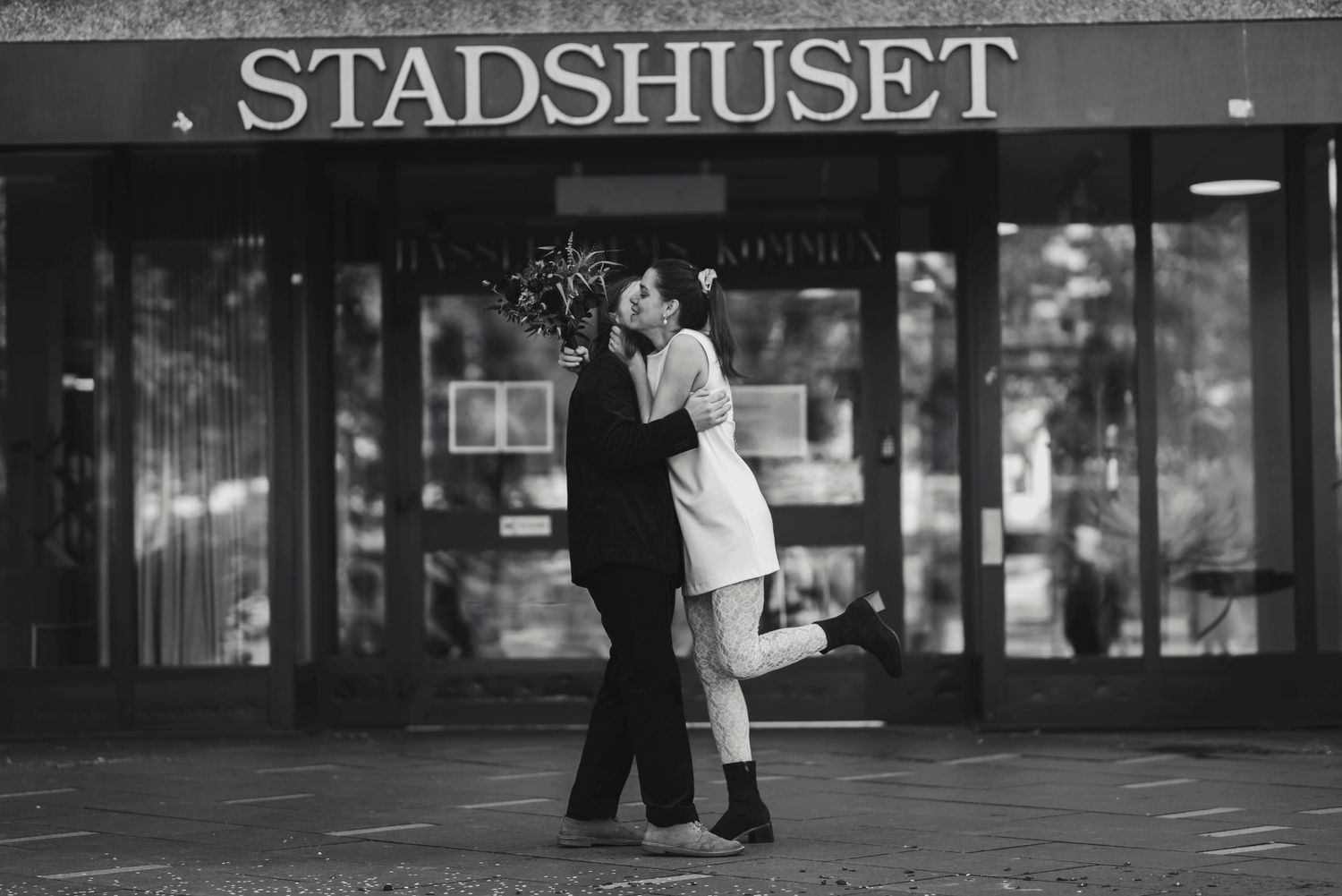 Romantic couple embracing outside Stadshuset building in black and white photography.