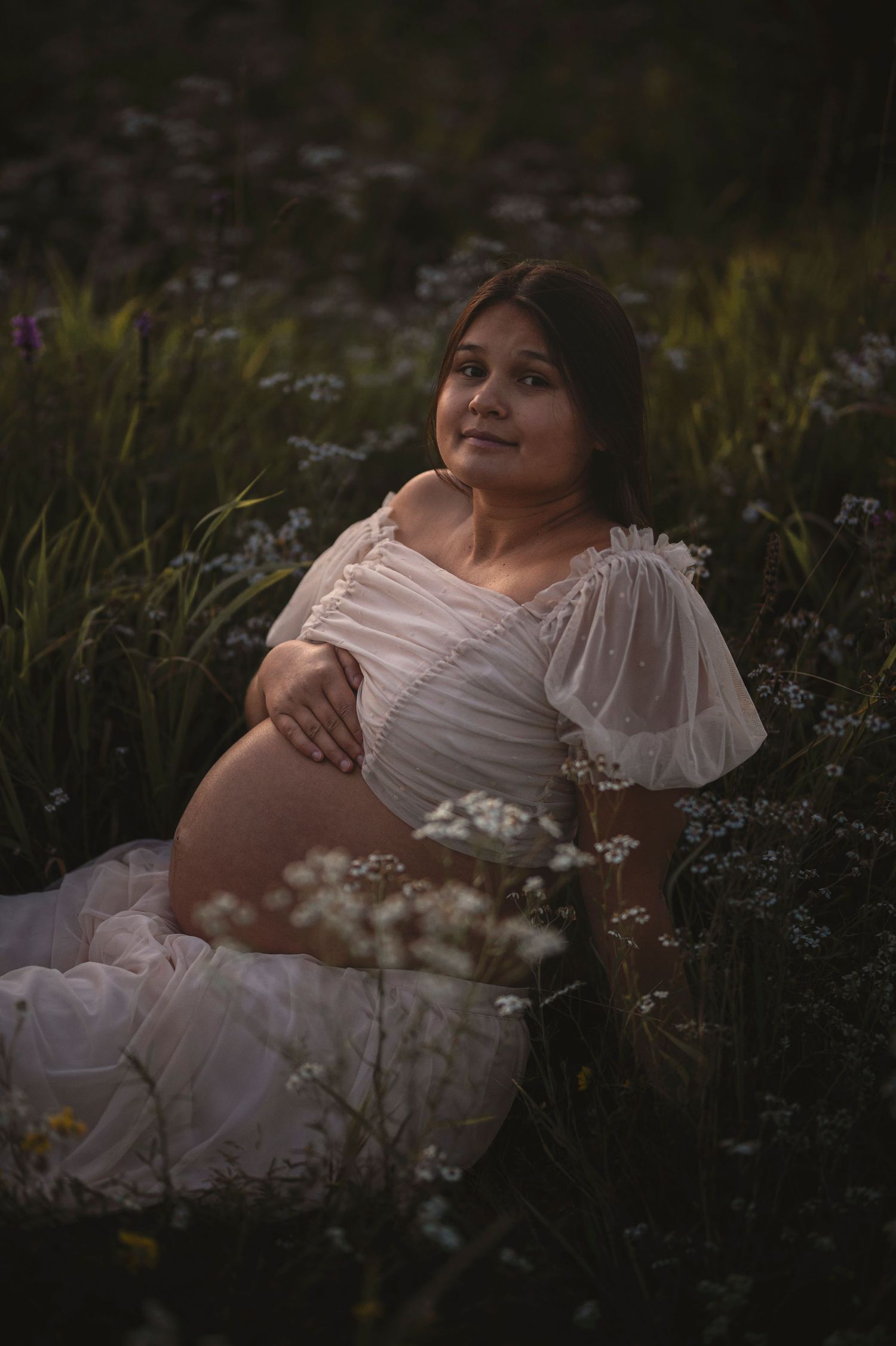 A peaceful maternity portrait amidst blooming wildflowers in soft evening light.