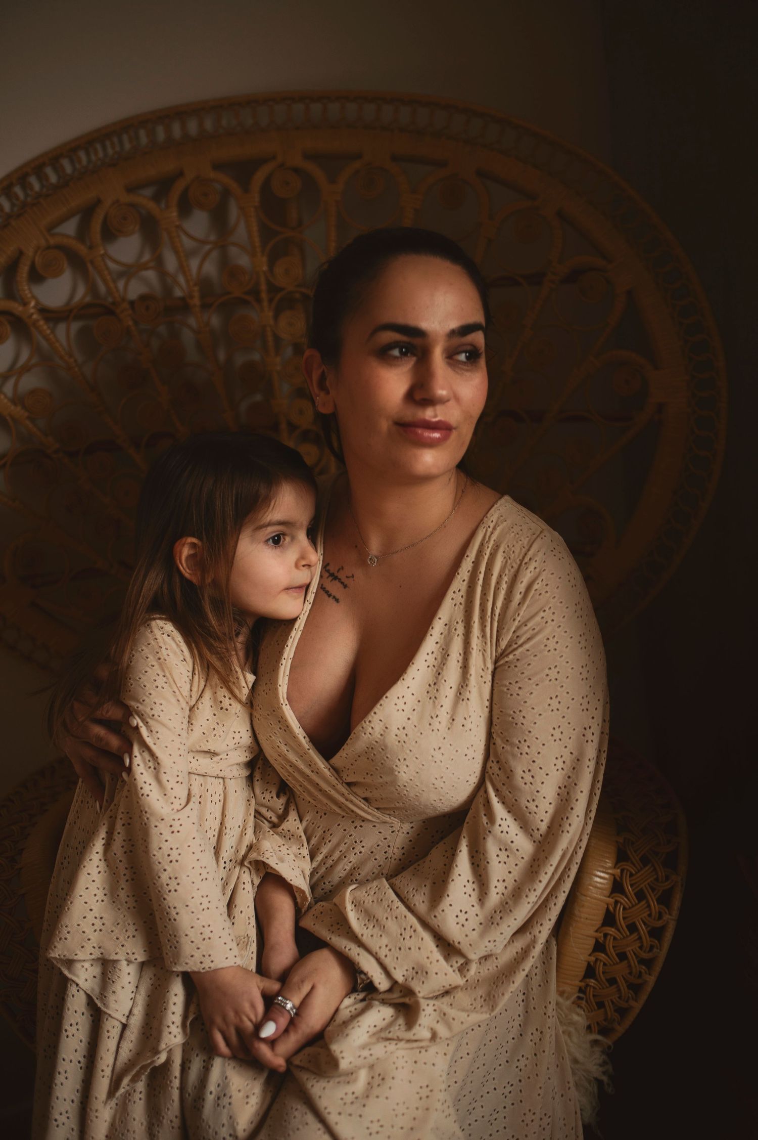 Warm-toned portrait features two people in matching cream dresses against wicker chair.