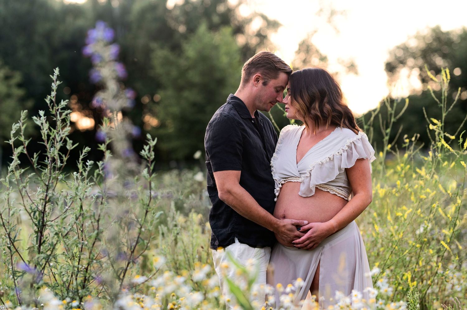 Gravidfotografering i Skåne med mjukt och känslosamt ögonblick i blomsteräng i gyllene solnedgång.