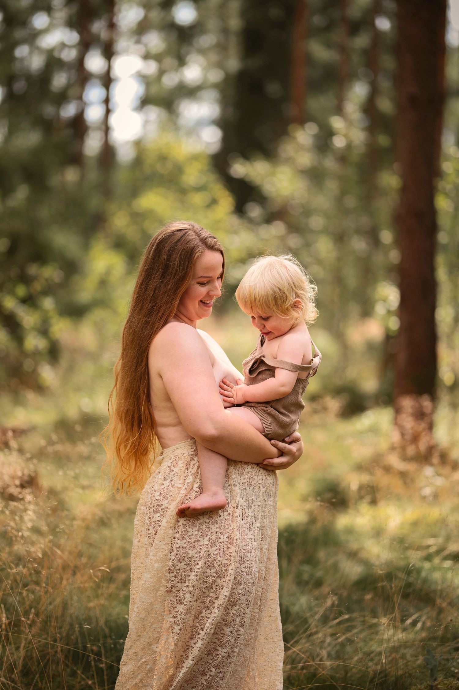 Moderskapsfotografering i Skåne med förälder som håller ett litet barn i spetsklänning i drömlik skogsmiljö.