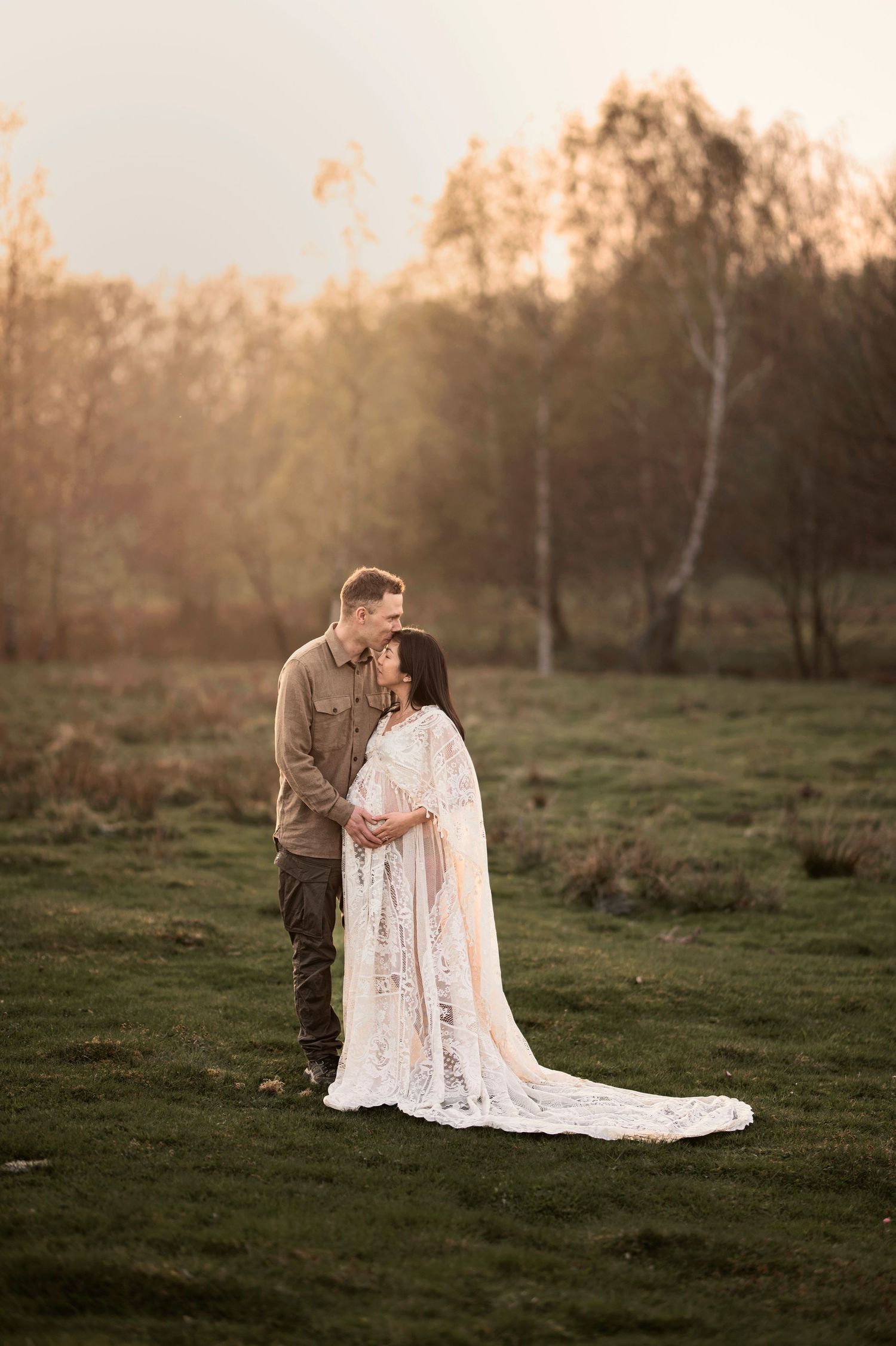 Gravid kvinna i spetsklänning och hennes partner under en gravidfotografering i Skåne vid solnedgånge