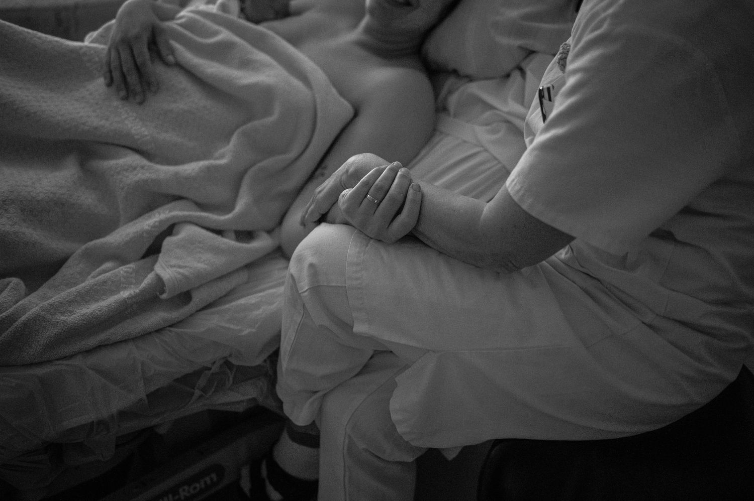 Gentle hands provide comfort and support during labor in this intimate black and white photograph.