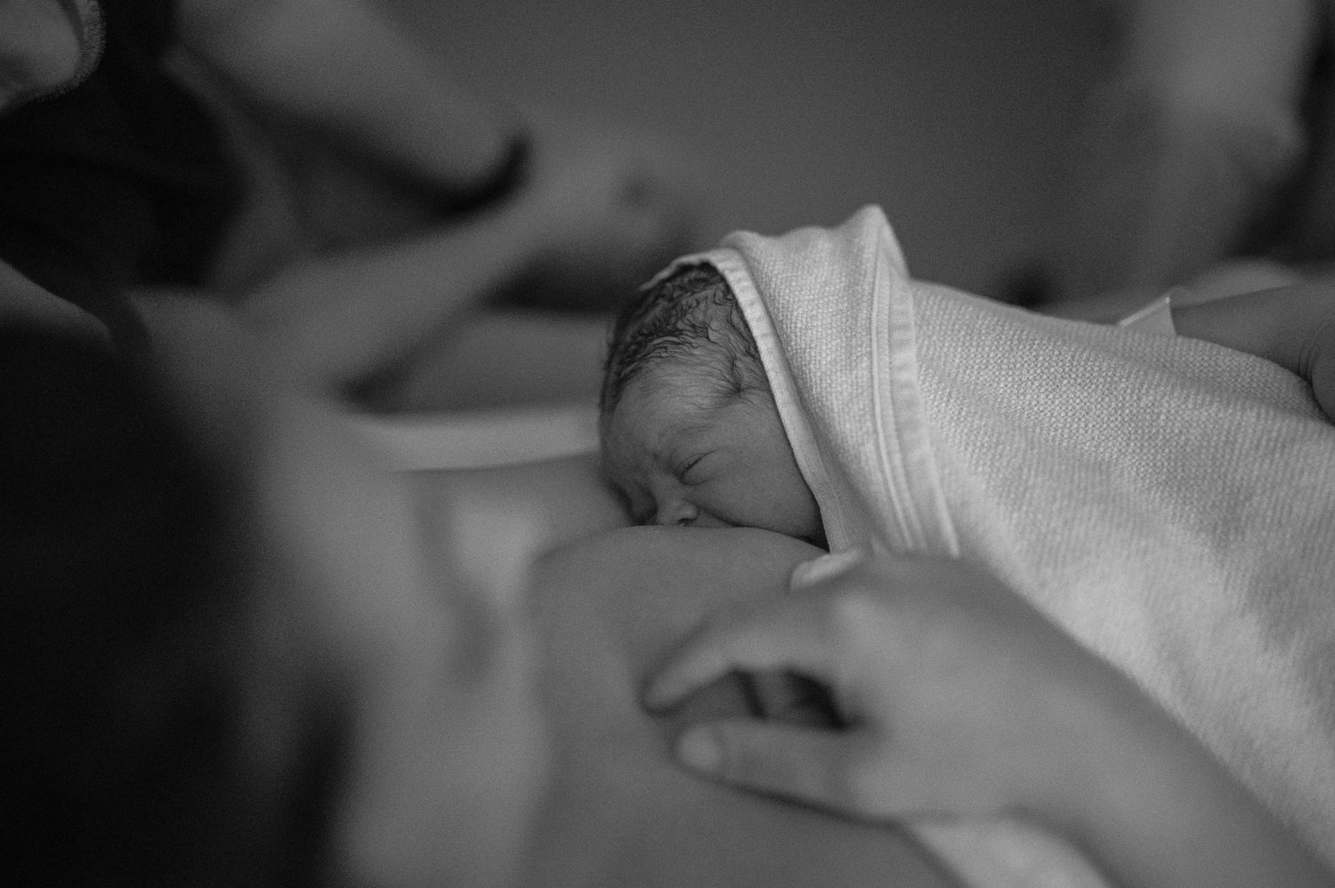 Svartvit förlossningsfotografering i Skåne med nyfödd bebis i famnen efter födseln.