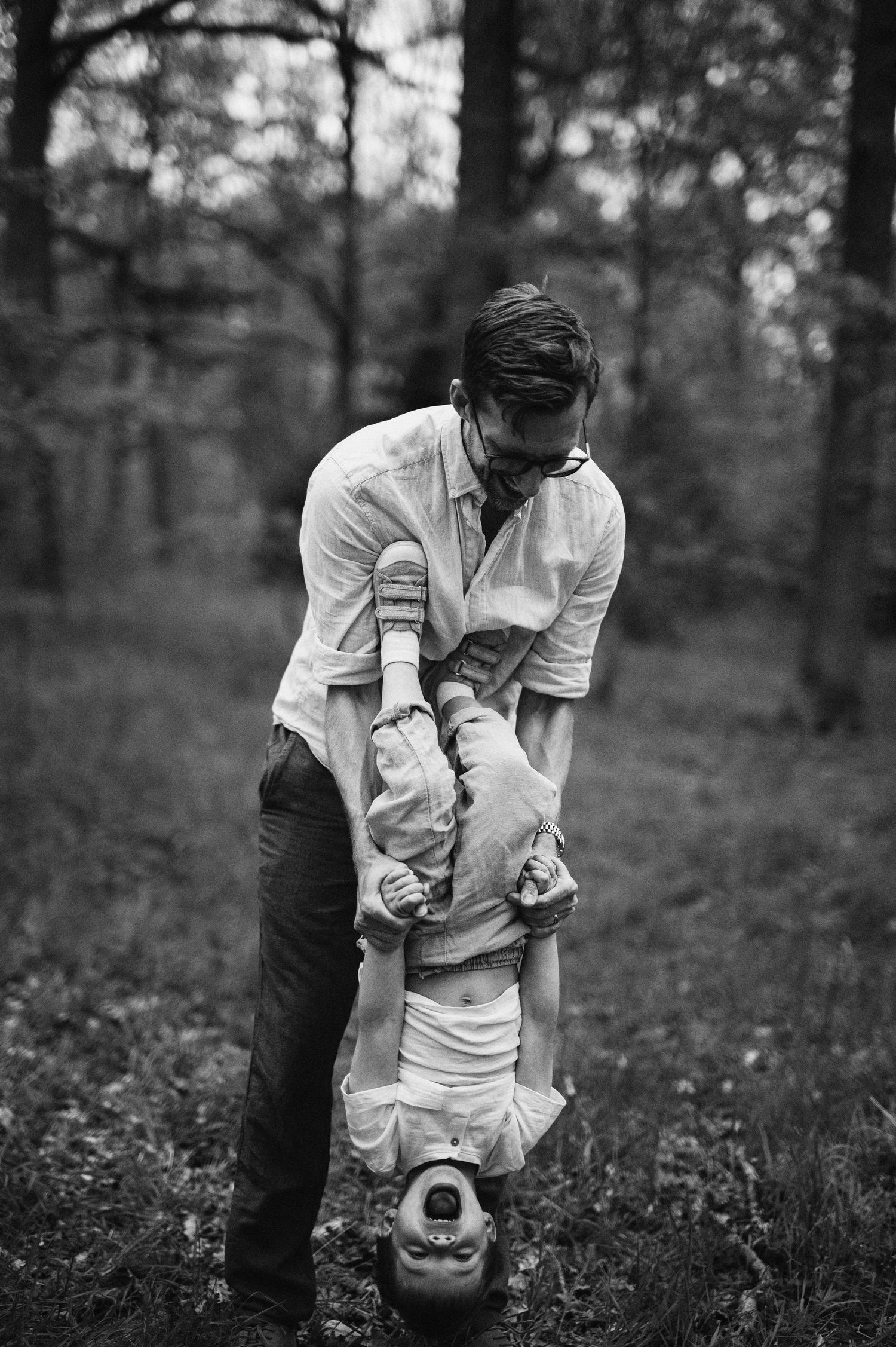 Familjefotografering i Skåne med pappa och barn i lekfullt ögonblick i skog i svartvitt ljus.