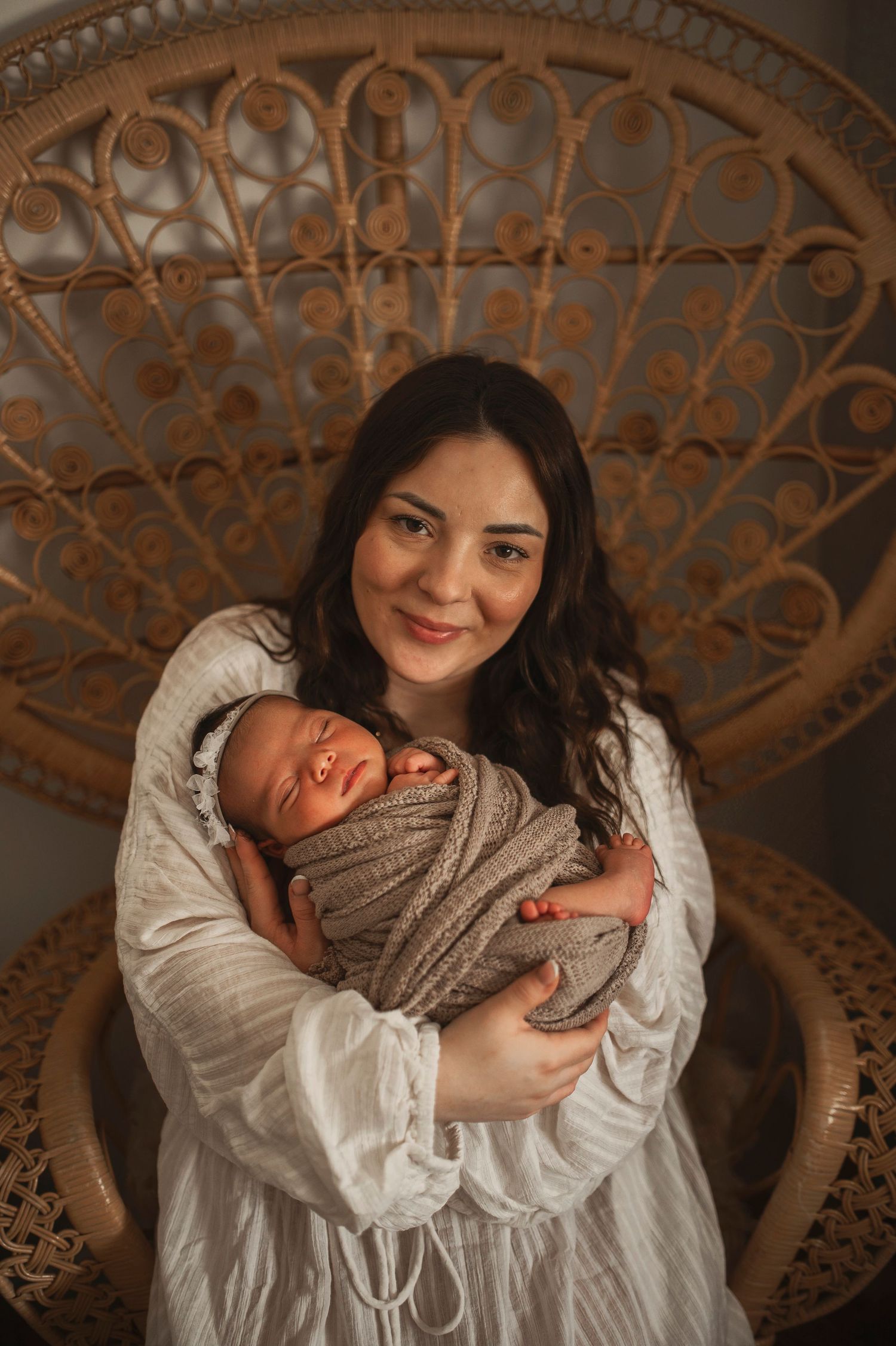 Mamma håller sin nyfödda bebis under en nyföddfotografering i Hässleholm i en rottingstol.