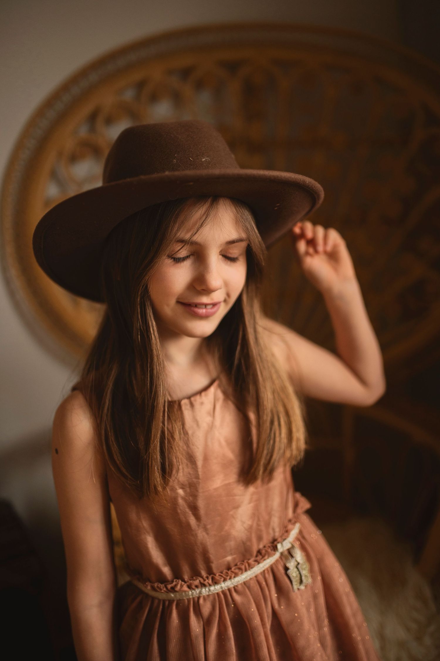 Dreamy portrait with brown dress and fedora against ornate wicker chair background.