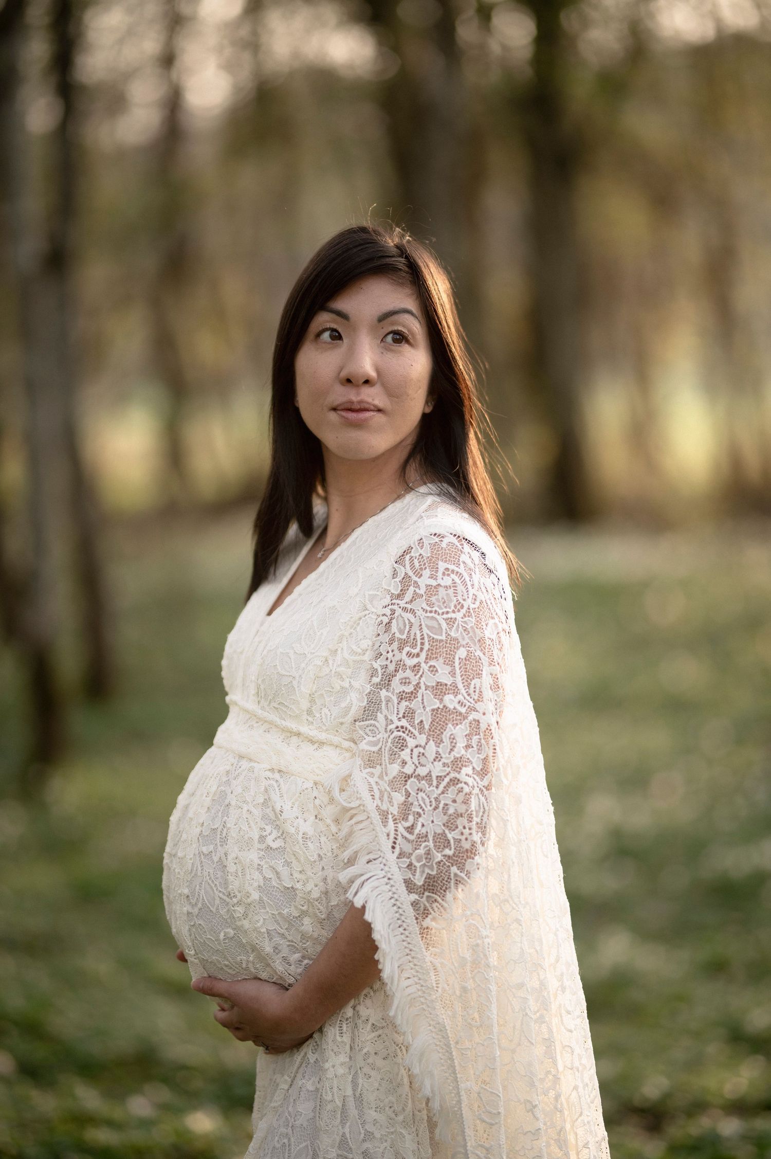 Gravid kvinna i spetsklänning fotograferad i skogen under en gravidfotografering i Skåne