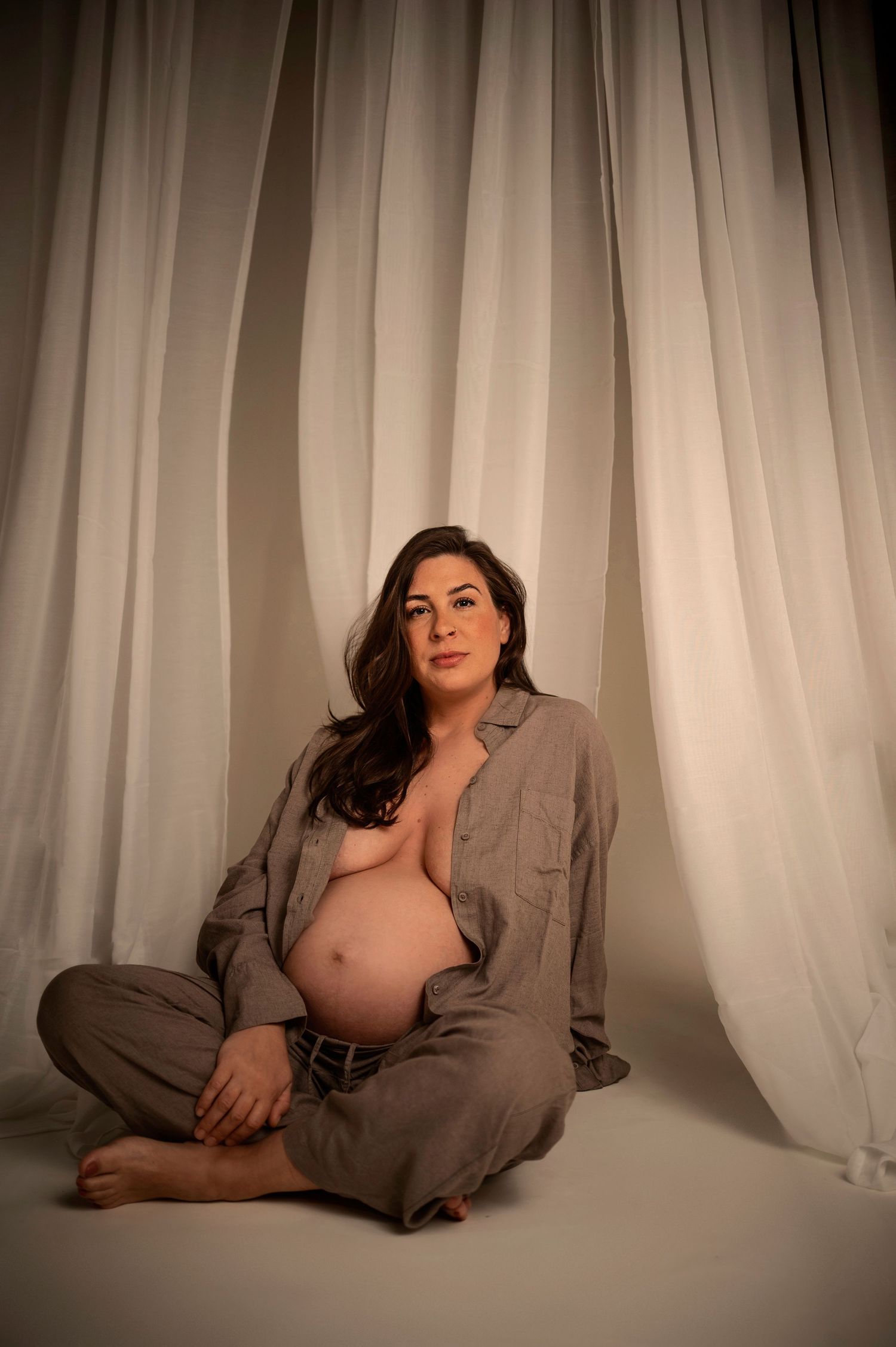 Gravid kvinna fotograferad i studio framför vita gardiner under en gravidfotografering.