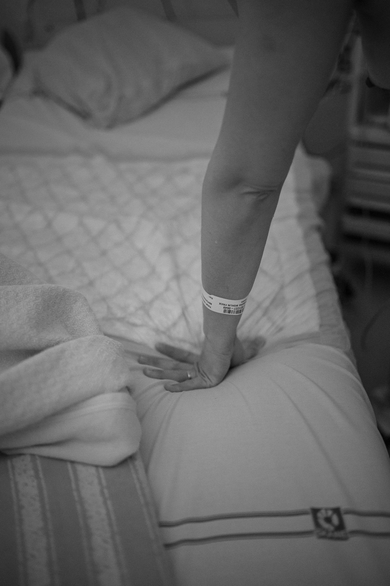 Svartvit förlossningsfotografering i Skåne med närbild på mammas hand under aktiv förlossning.