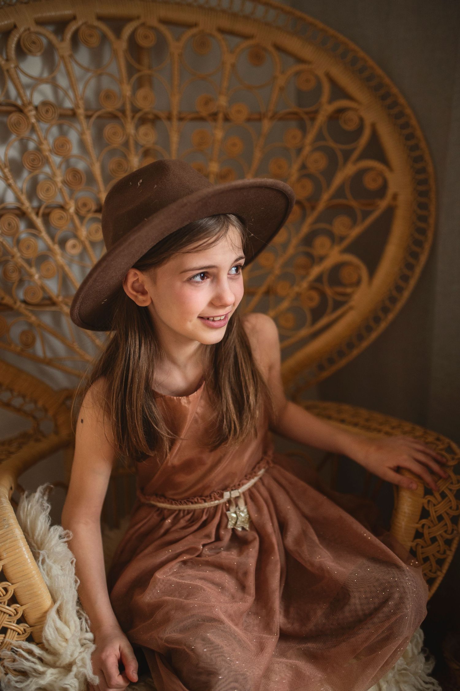 A brown dress and fedora create a vintage aesthetic against an ornate wicker chair backdrop.