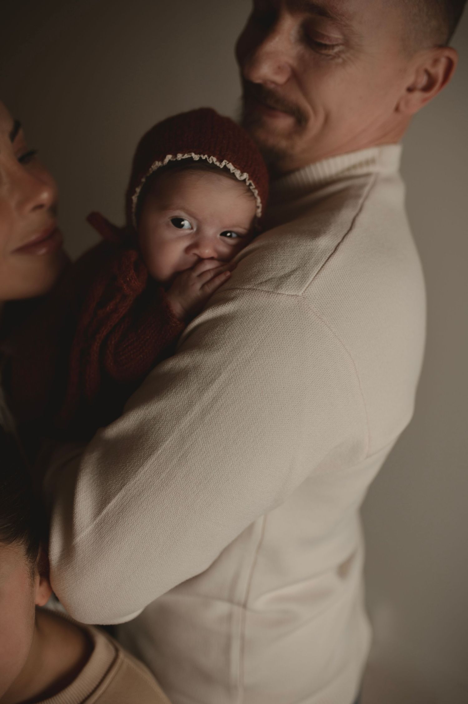 Tender family moment with baby in burgundy outfit and knit hat.