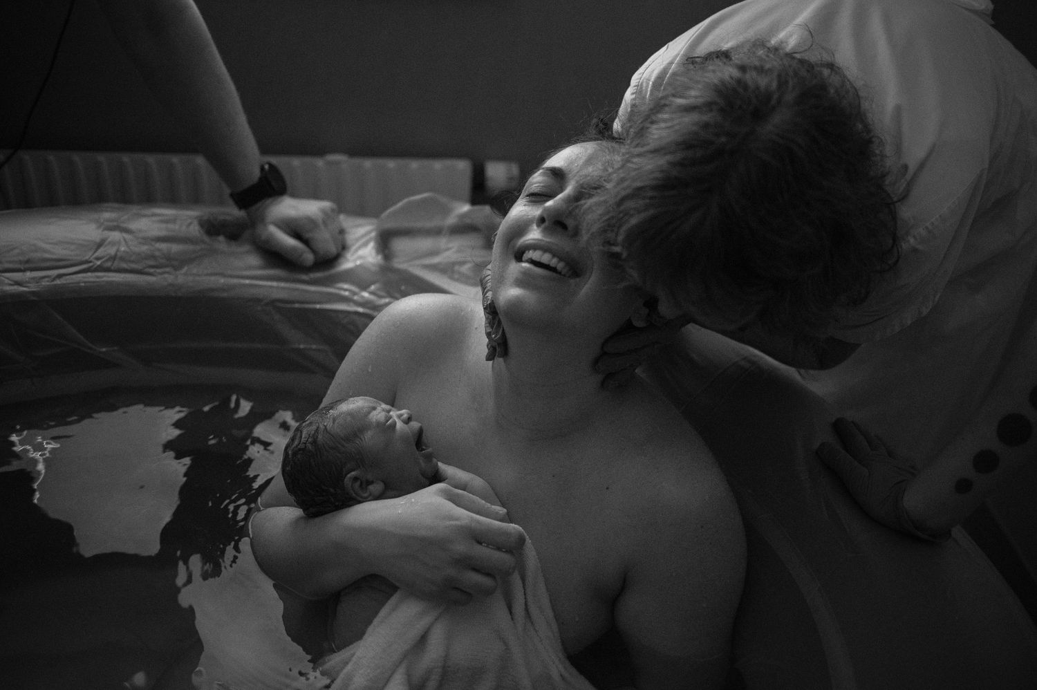 Svartvit förlossningsfotografering i Skåne med mamma som håller sin nyfödda bebis i en vattenförlossning.