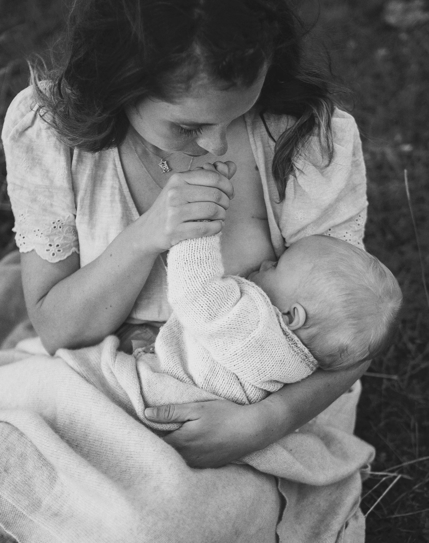 Amningsfotografering i Skåne med mamma som kysser nyfödd bebis hand i svartvitt ljus.
