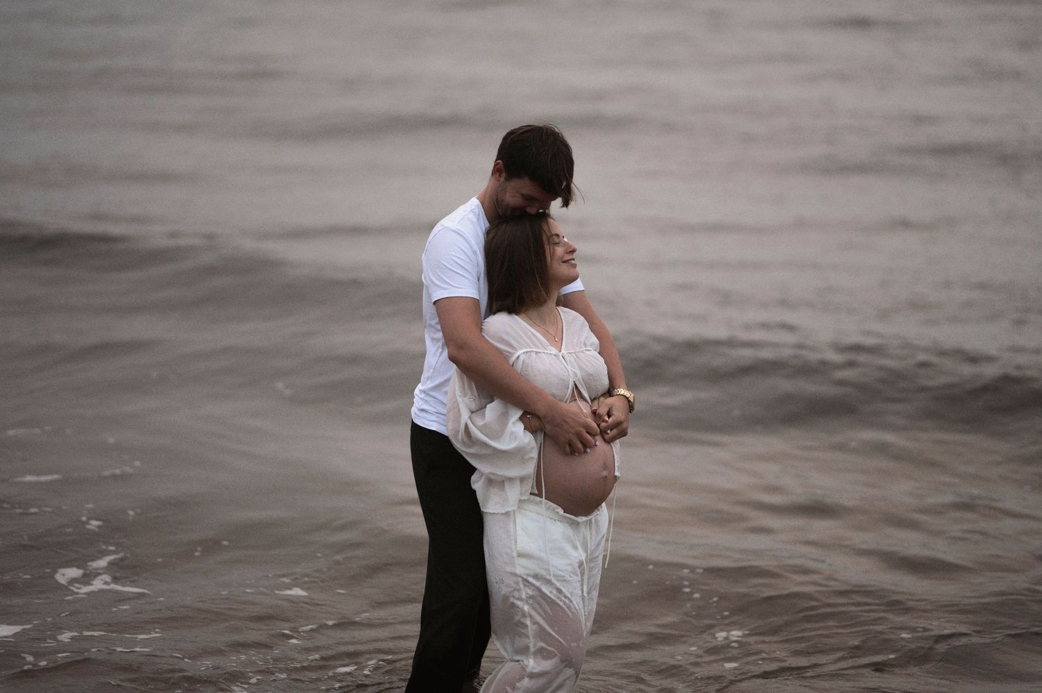 Intimate beach portrait with white dress against moody ocean backdrop.