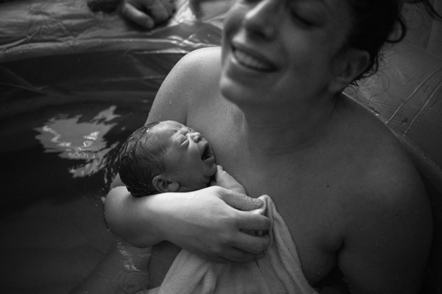 A tender black and white photograph captures the intimate moment of skin-to-skin contact between parent and newborn.