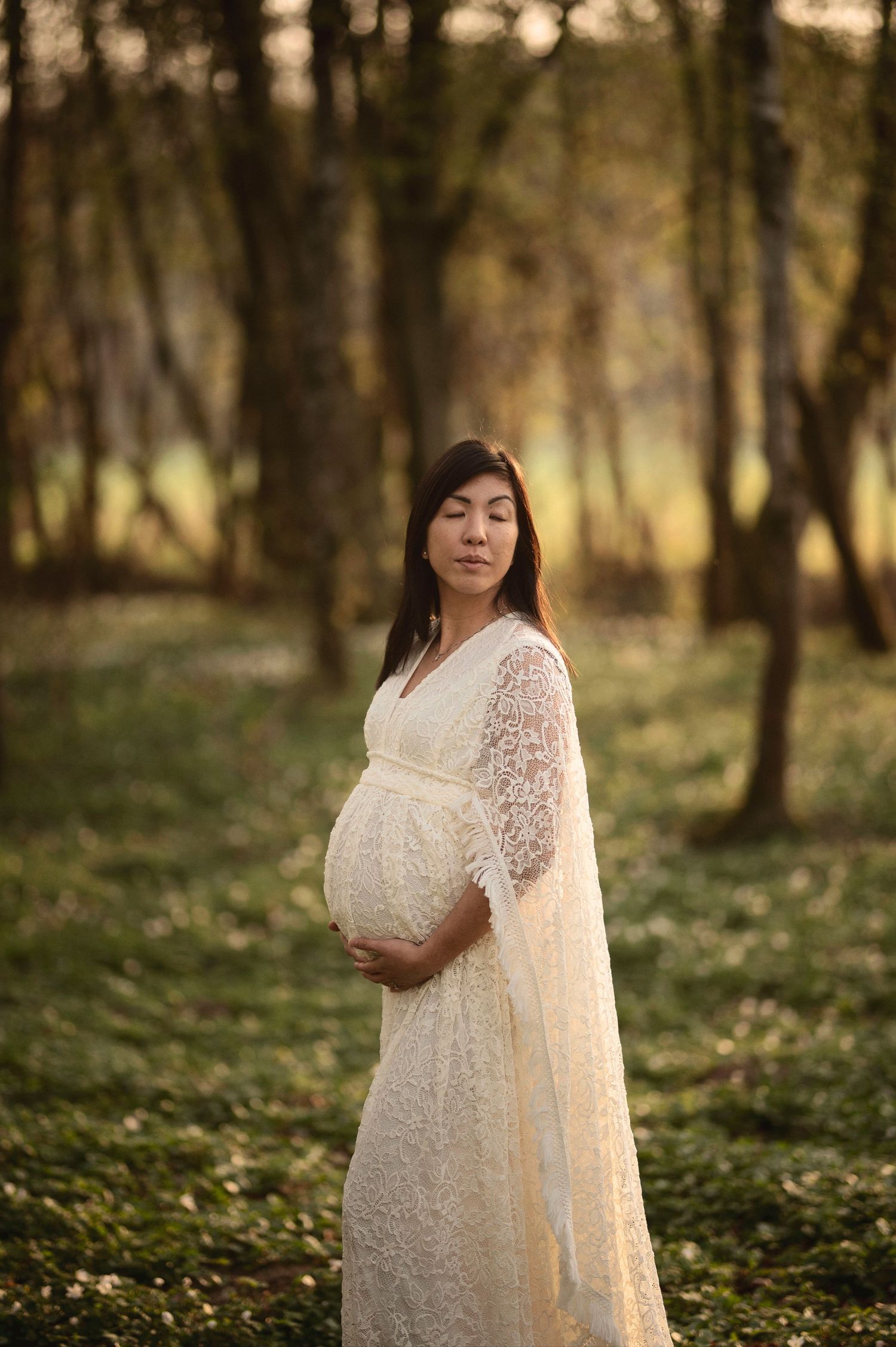 Blivande mamma fotograferad i en solbelyst skog under en gravidfotografering i Skåne