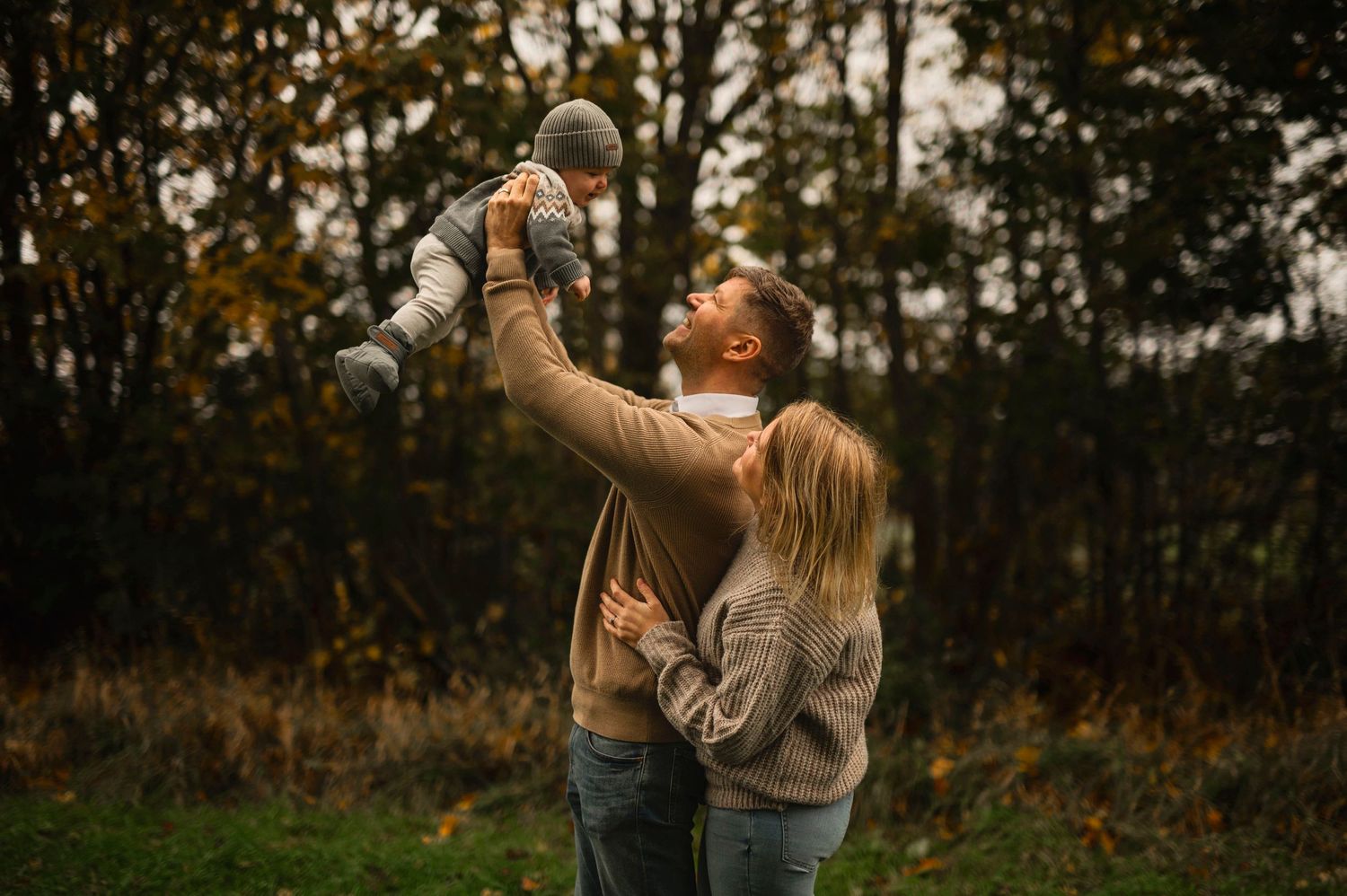 Parent lifts child joyfully in the air during autumn outdoor photo session.