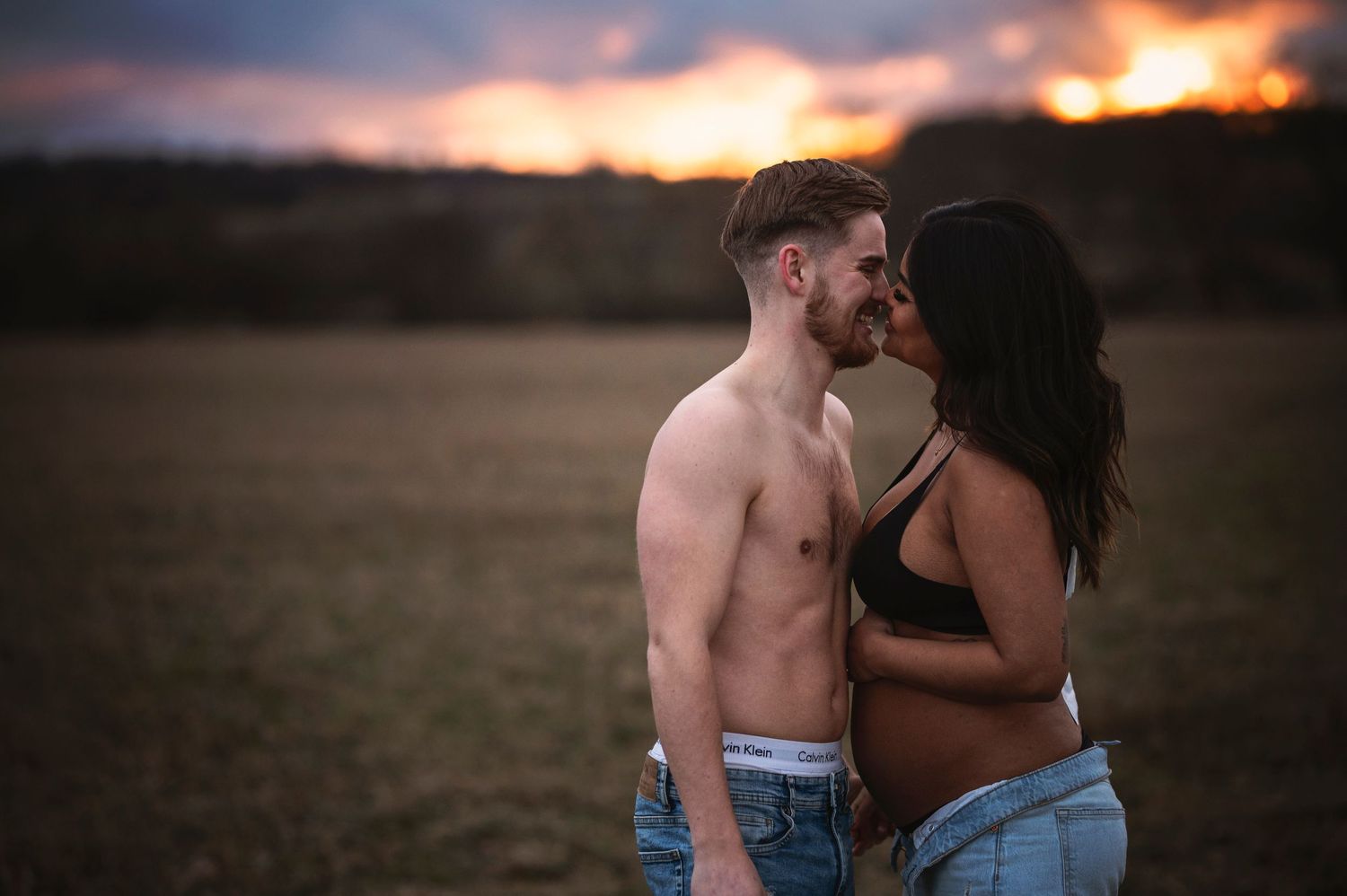 A couple embraces during their outdoor maternity photoshoot at sunset.