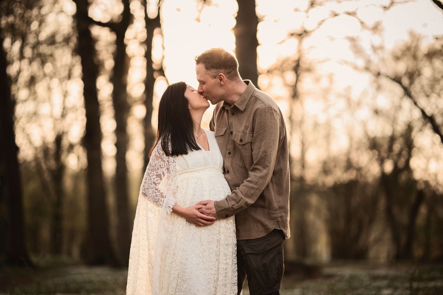 Blivande föräldrar omfamnar varandra i en solbelyst skog under en gravidfotografering i Skåne.