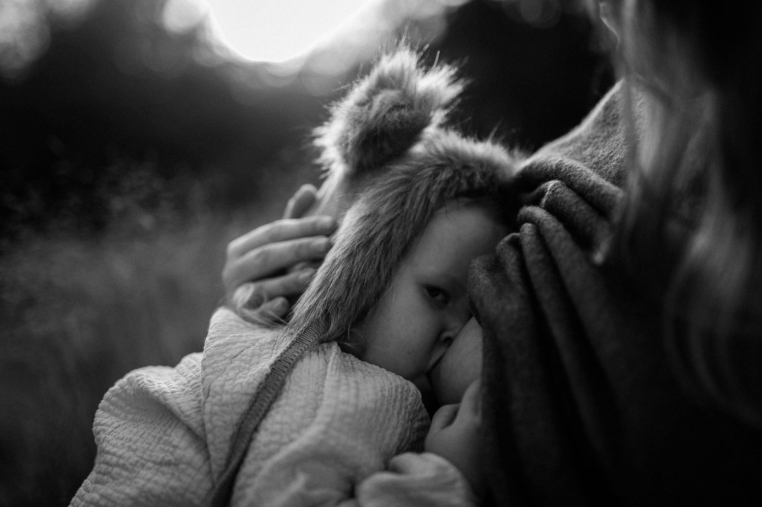 Amningsfotografering i Skåne med bebis i björnmössa som ammar hos mamma i svartvitt utomhusljus.