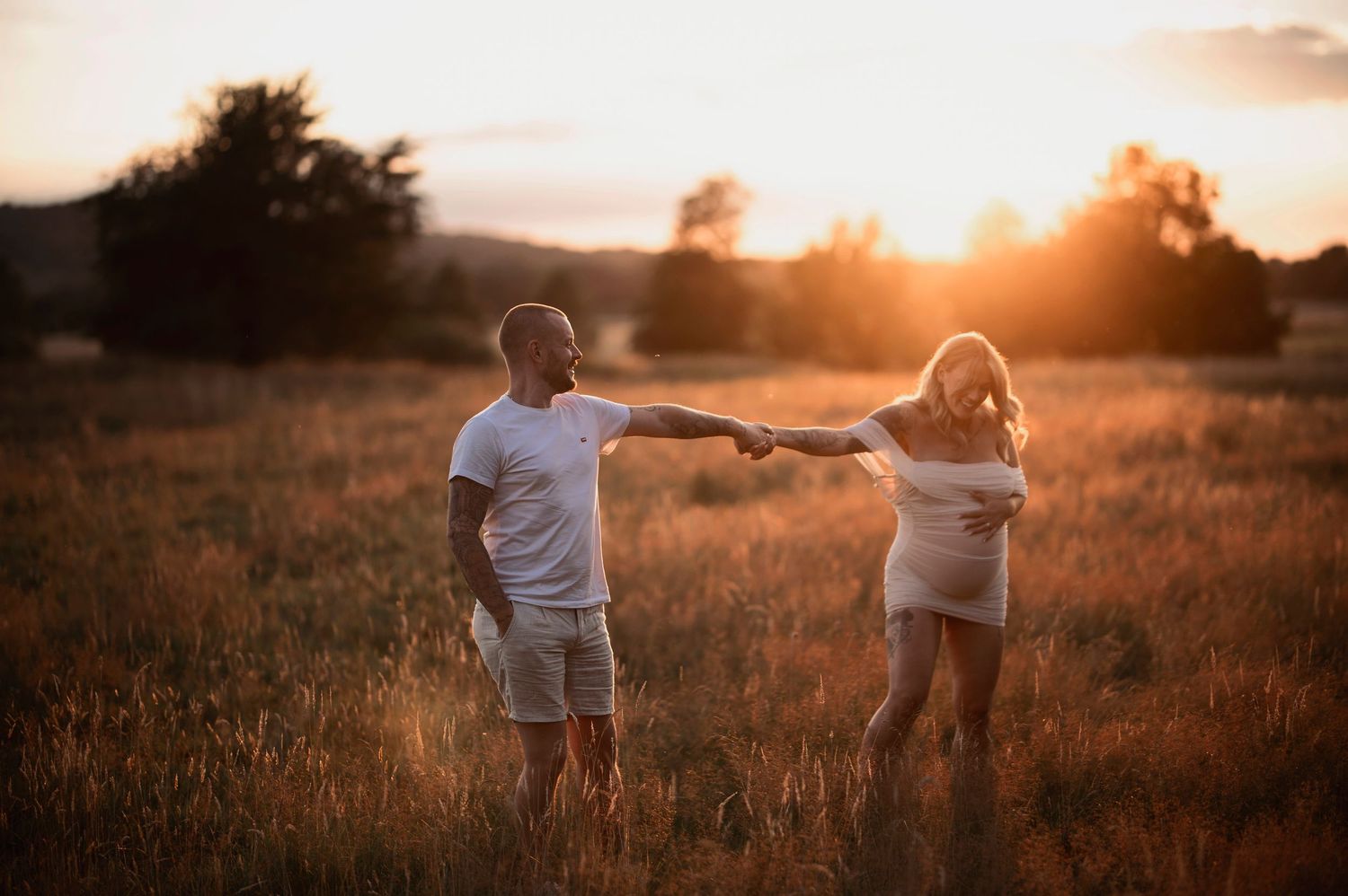Gravidfotografering i Skåne med blivande föräldrar som dansar i ett gyllene fält vid solnedgången.