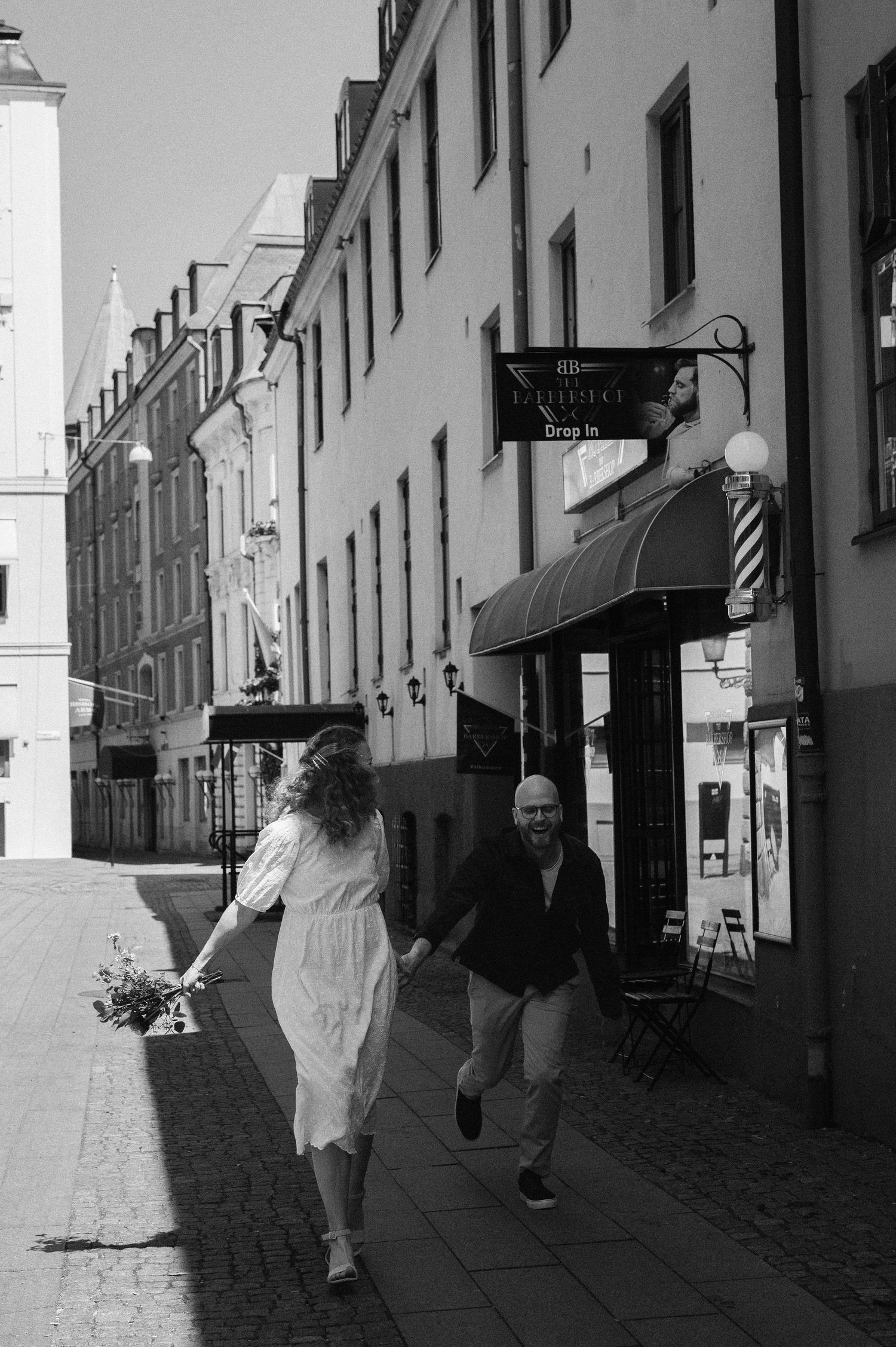Couple holding hands walking on sunny European cobblestone street.