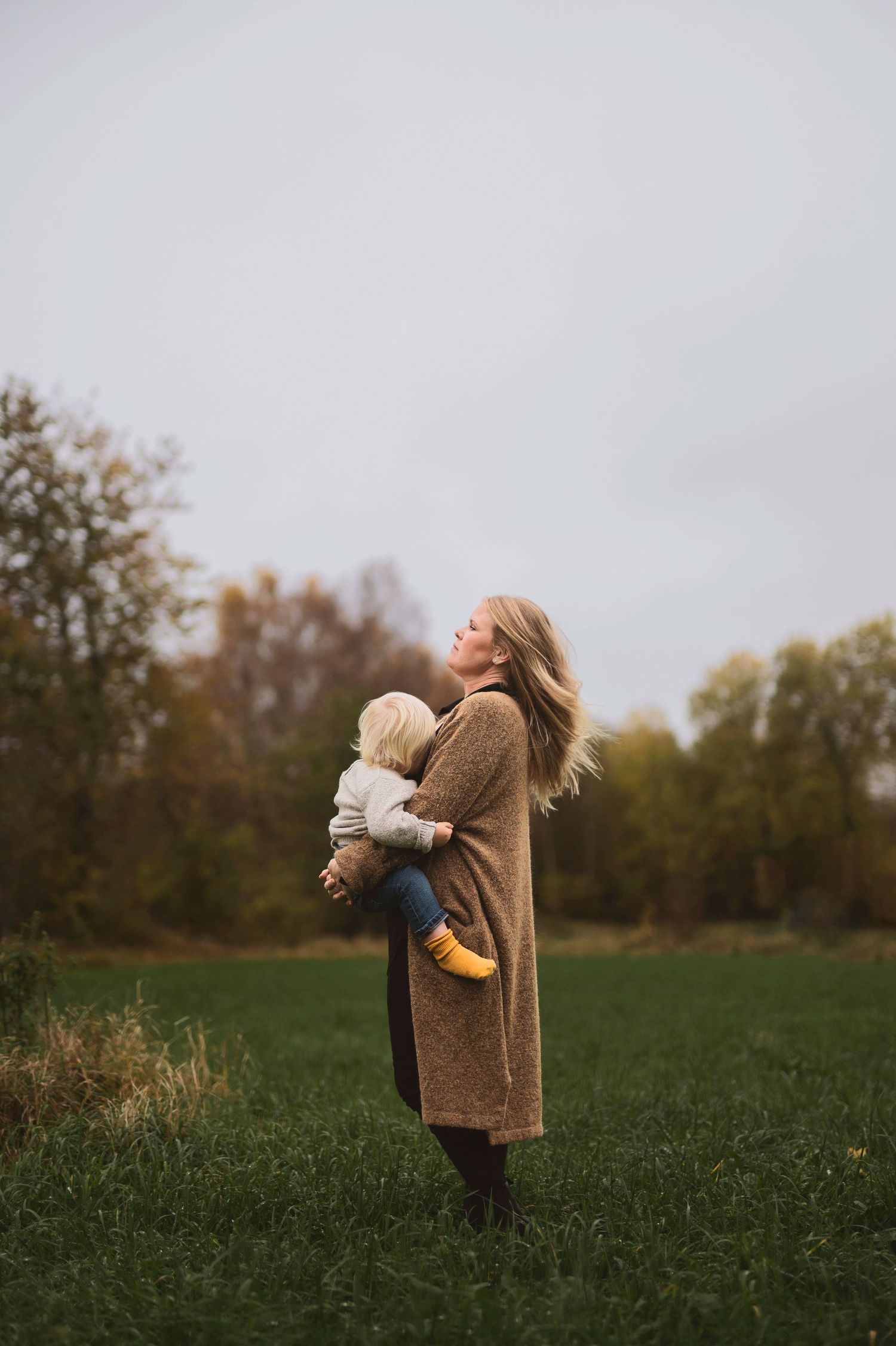 Amningsfotografering i Skåne med mamma som håller sitt barn i höstlandskap i mjukt naturligt ljus.