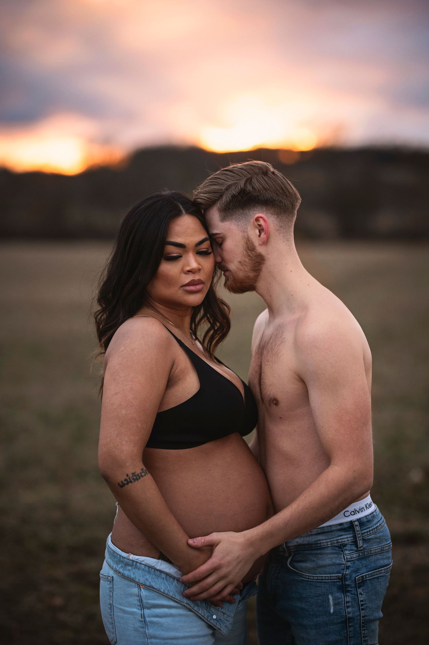 An intimate maternity portrait captured against a warm sunset backdrop.