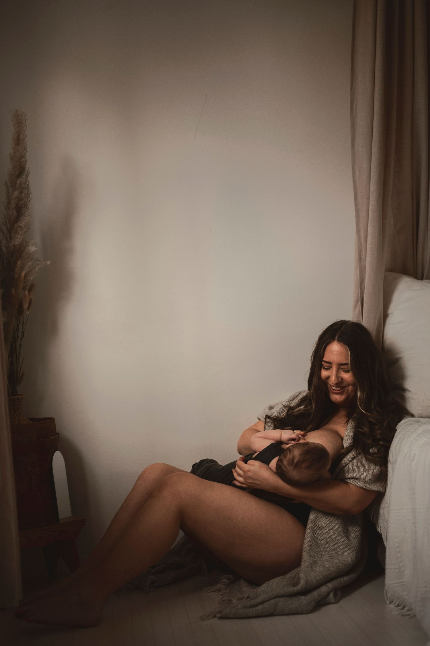 Mother smiling warmly while breastfeeding her newborn baby in a softly lit bedroom.
