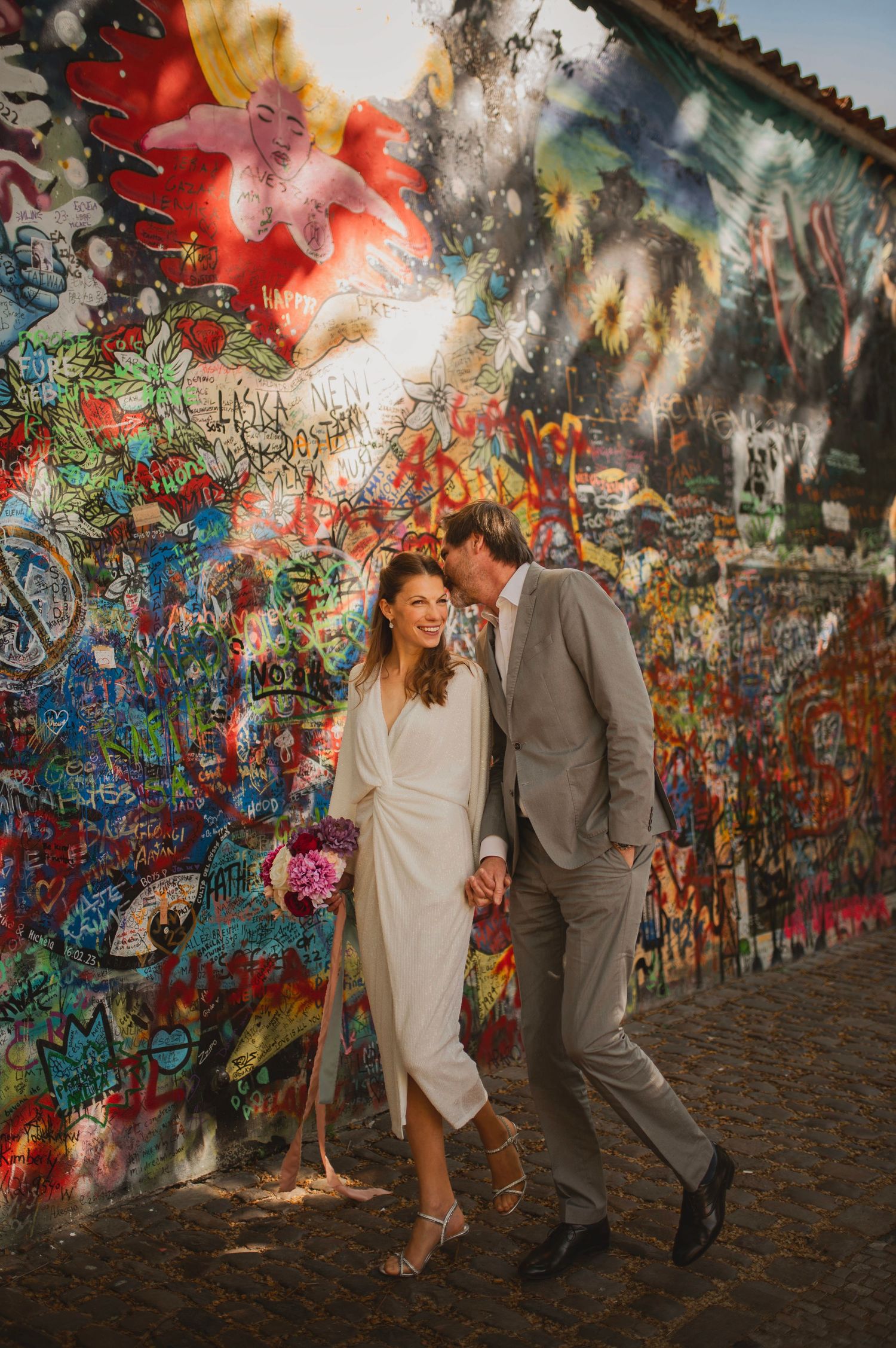 Bröllopsfotografering i Prag med brudpar som skrattar vid John Lennon Wall i färgstark stadsmiljö.