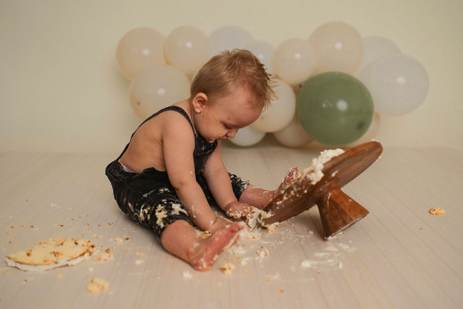 A playful moment captured during a cake smash session with balloons and scattered crumbs.