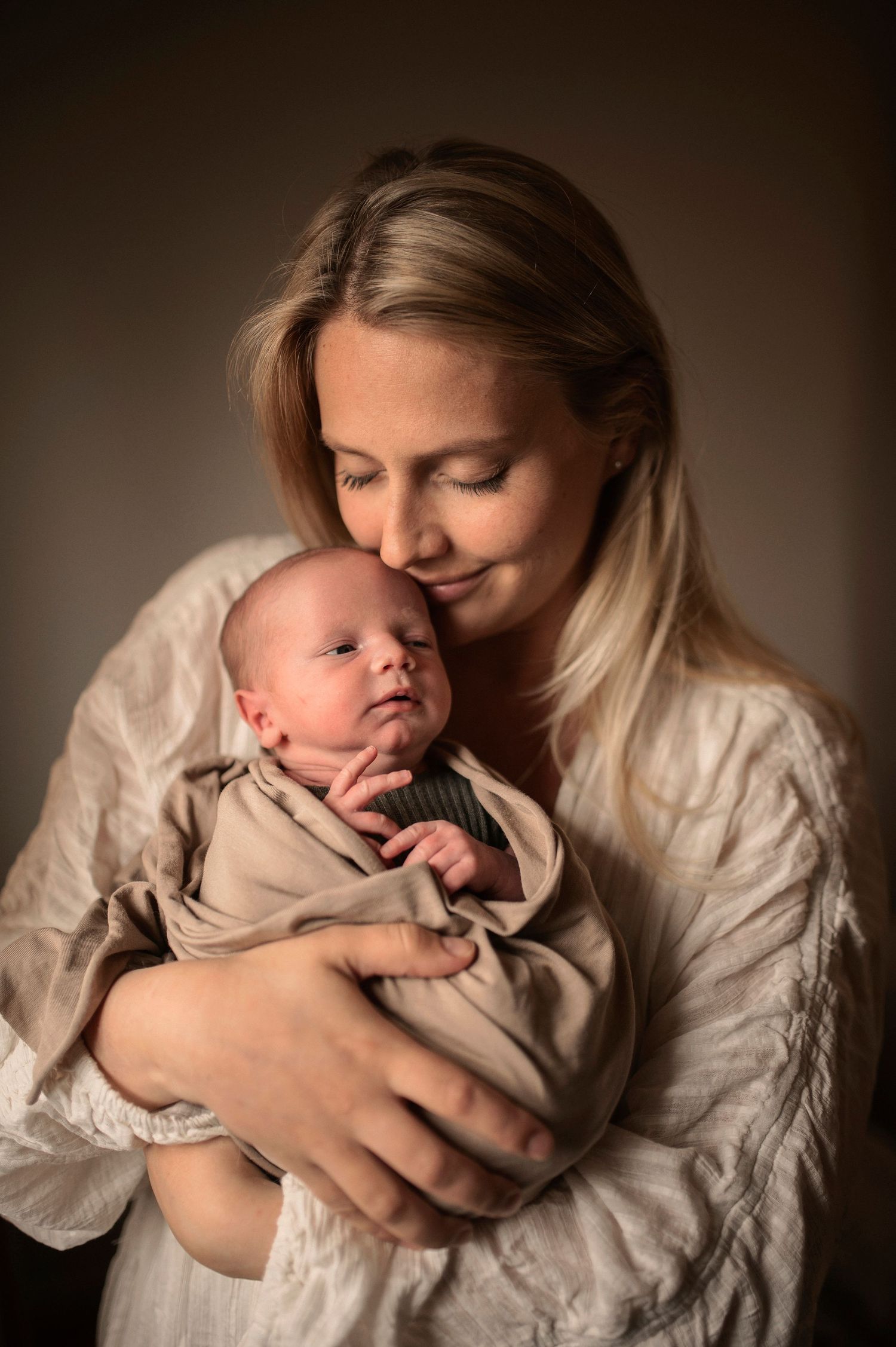 Mamma håller sin sovande nyfödda bebis under en nyföddfotografering i Hässleholm.