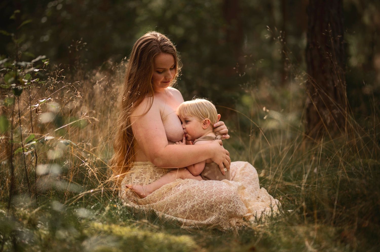 Moderskapsfotografering i Skåne med förälder som håller ett litet barn i spetsklänning i drömlik skogsmiljö.